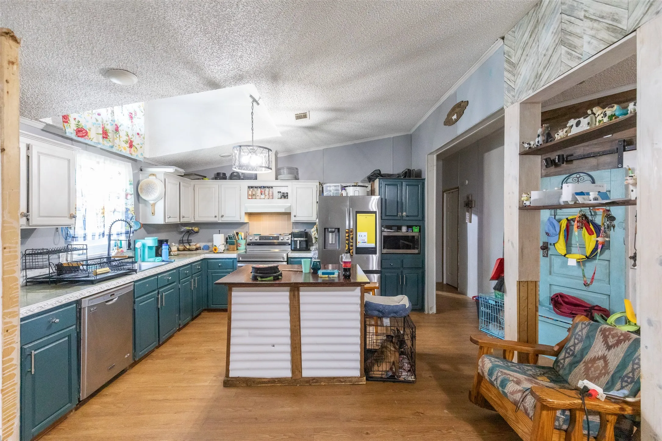 Kitchen featuring two-tone cabinetry with white upper and teal lower cabinets, stainless steel appliances, and a central island with wood-finish countertop