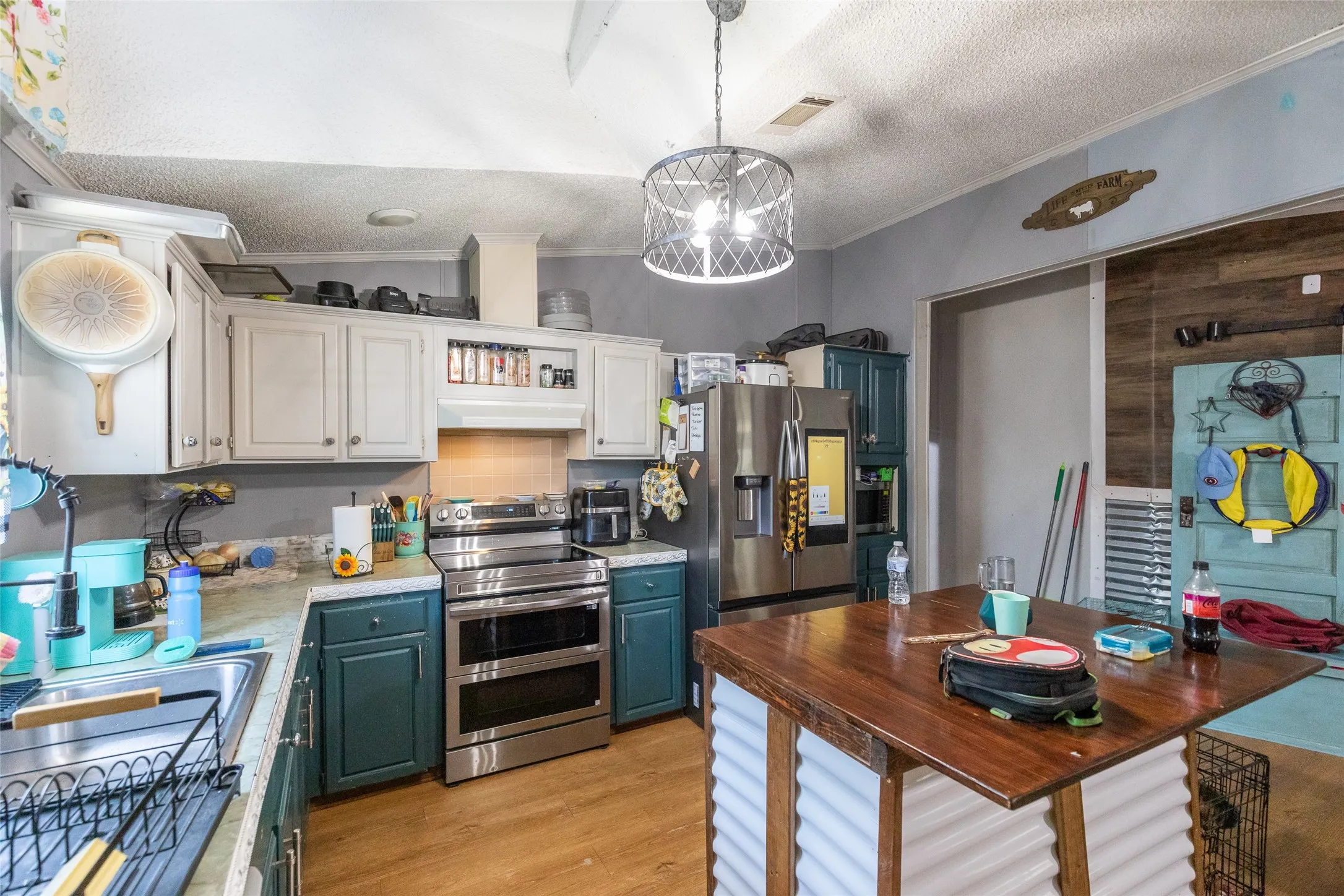 Kitchen featuring two-tone cabinetry with white upper and teal lower cabinets, stainless steel appliances, a double basin sink, and wood-finish flooring