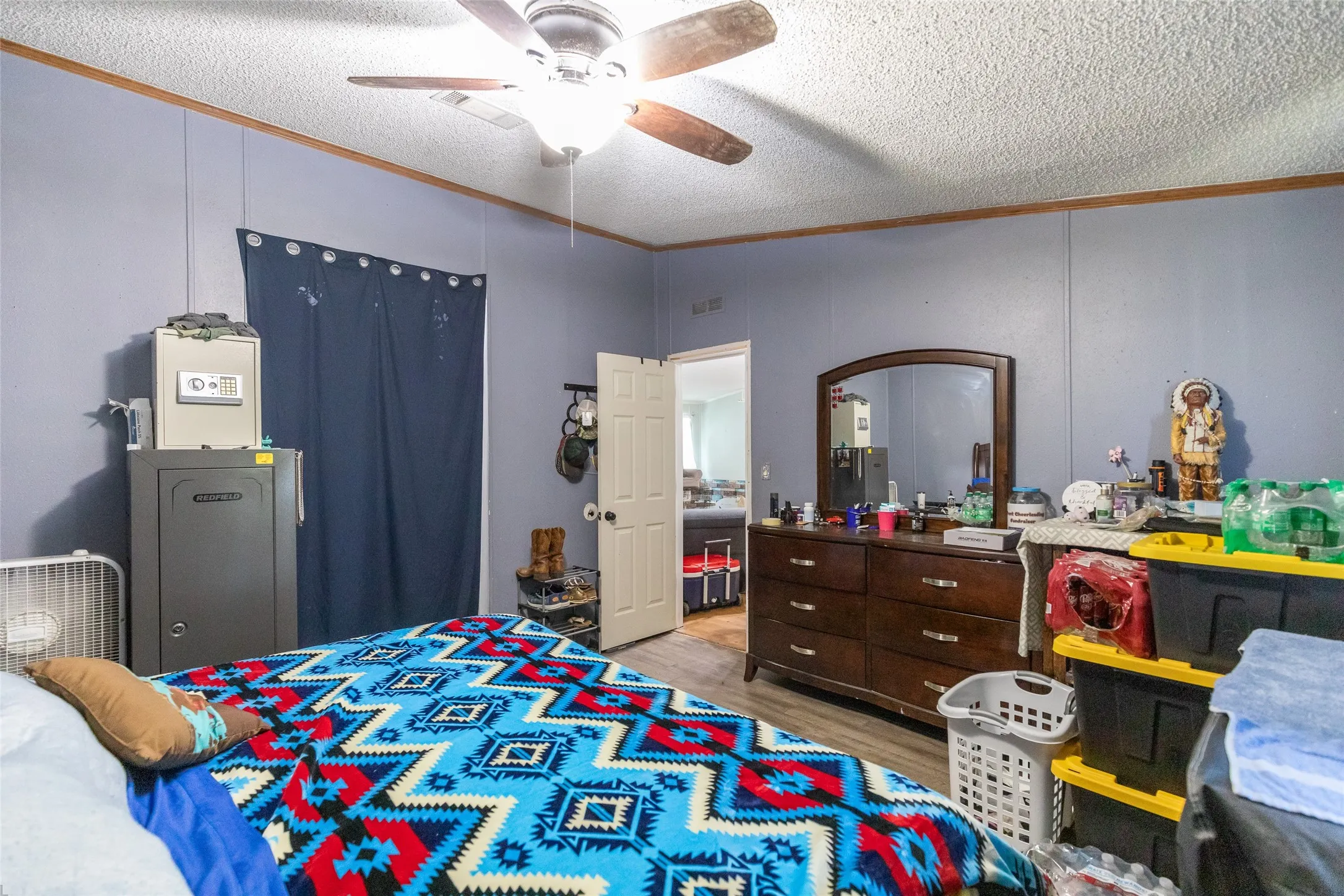 Interior room featuring light blue walls, wood-finish flooring, a white ceiling with a textured finish, and a ceiling fan with wood-finish blades