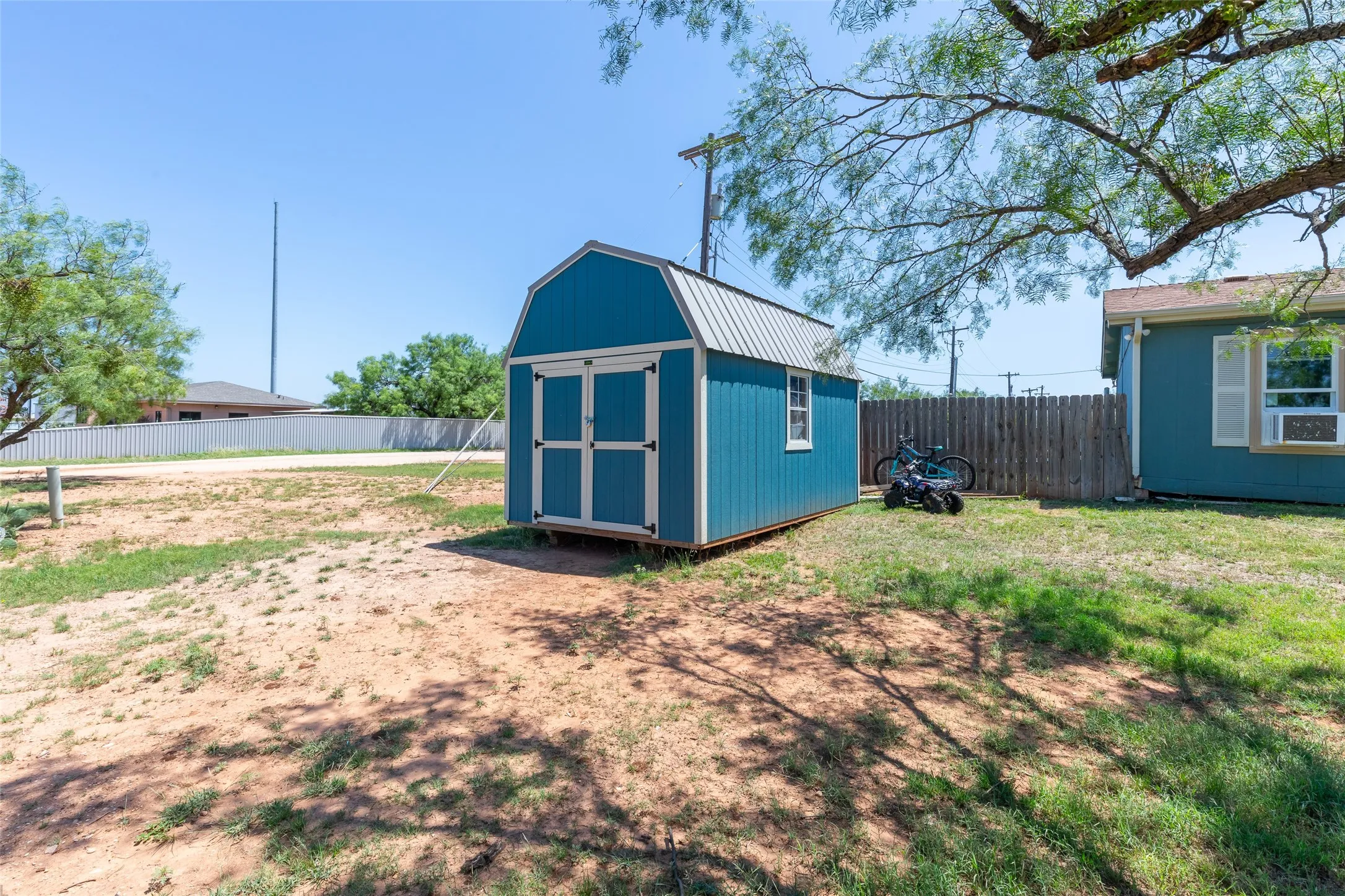 Detached blue storage shed with white trim and a metal gambrel roof