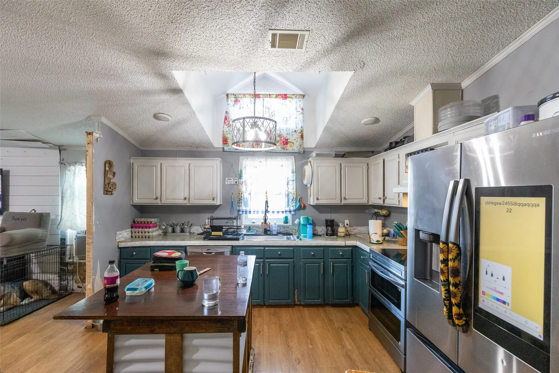 Kitchen featuring wood-finish flooring, white upper cabinetry, teal lower cabinetry, and stainless steel appliances