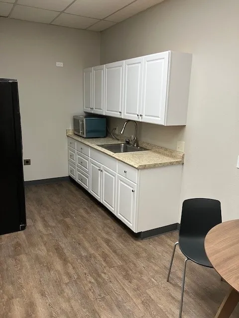 Kitchenette featuring wood-finish flooring, white shaker-style cabinetry, a stainless steel sink with a gooseneck faucet, and light-toned speckled countertops