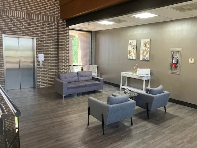 Lobby area featuring wood-finish flooring, brick accent wall, stainless steel elevator doors, large windows, and recessed ceiling lighting