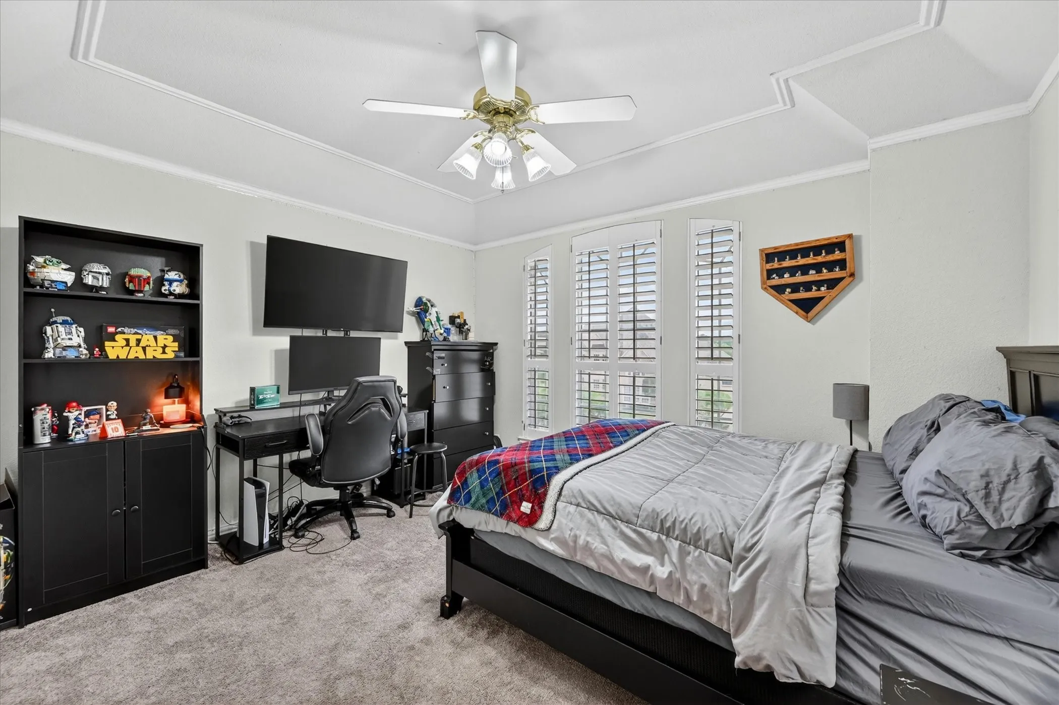 Spacious room featuring a tray ceiling with crown molding, three tall windows with plantation shutters, and light gray wall paint