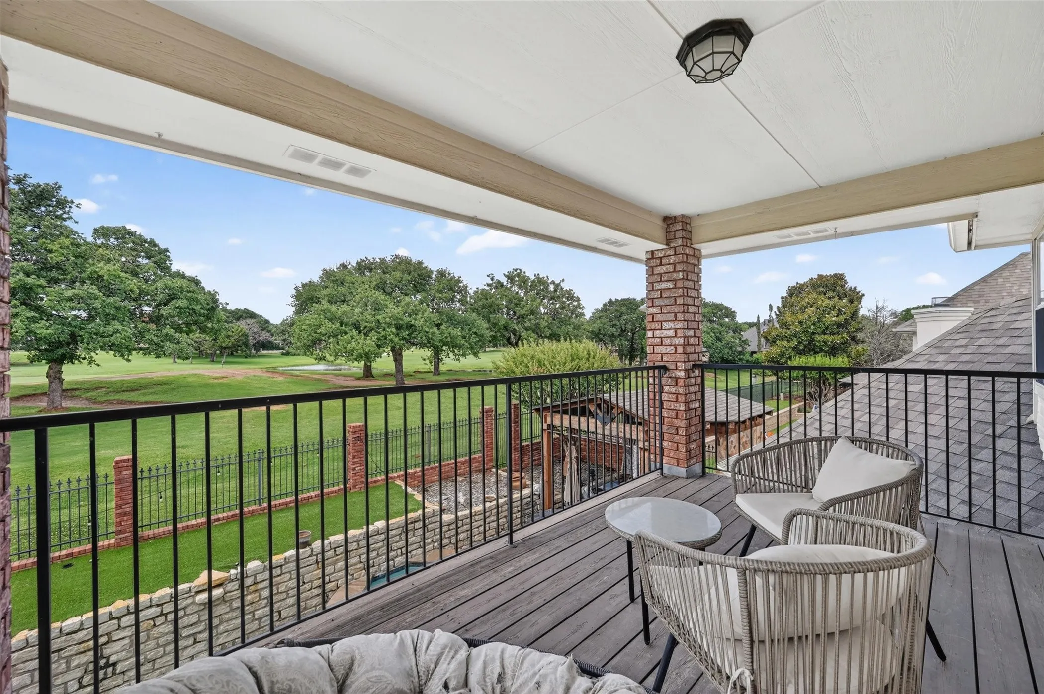Covered balcony featuring wood-finish flooring, a brick support column, and black metal railings overlooking a golf course