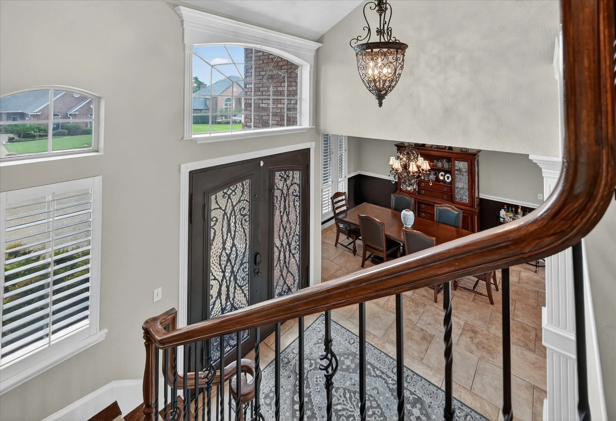 Two-story foyer with decorative wrought iron entry doors, arched transom windows, and a classic chandelier