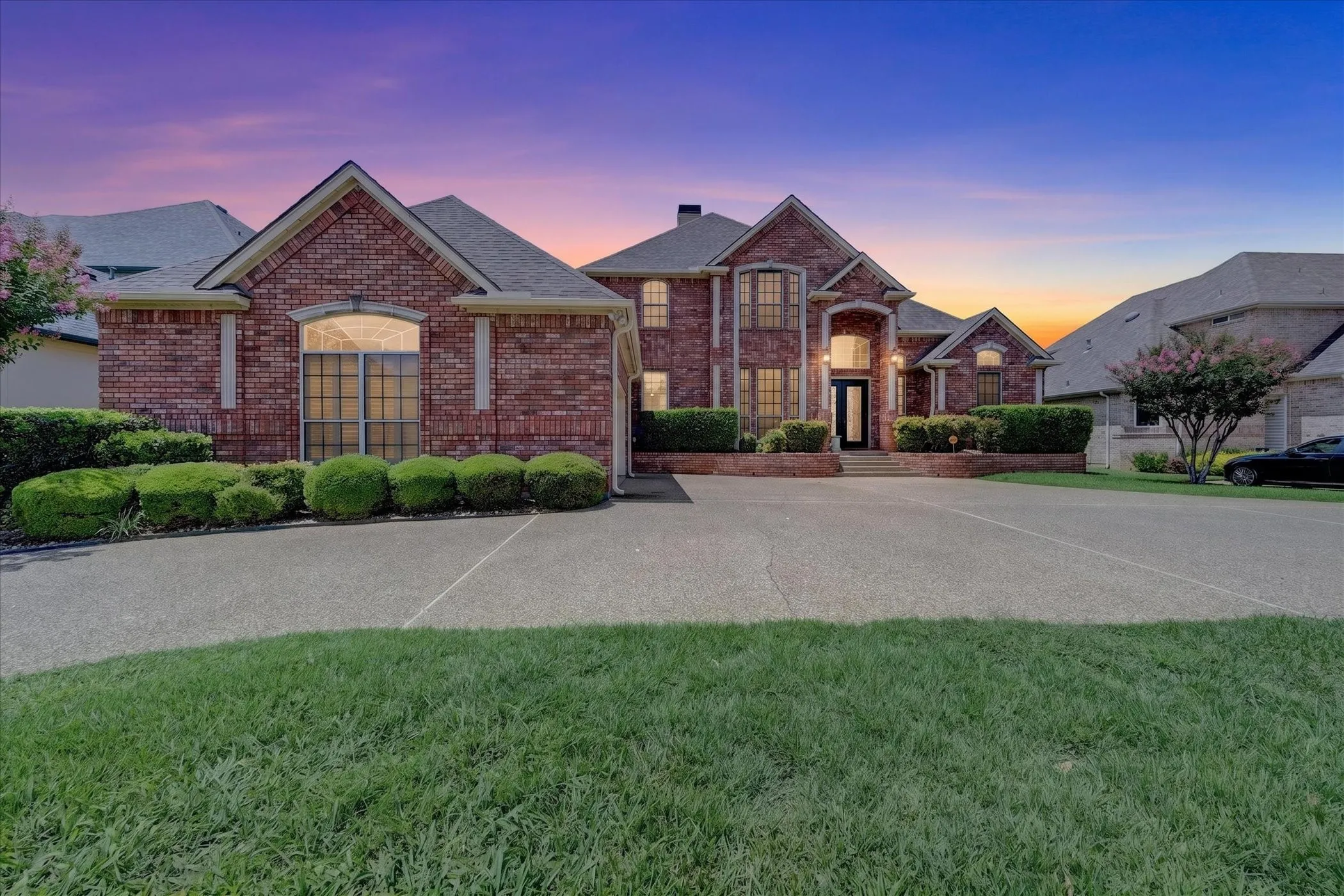 Grand brick residence featuring a prominent entryway, arched windows, a circular drive, and mature landscaping