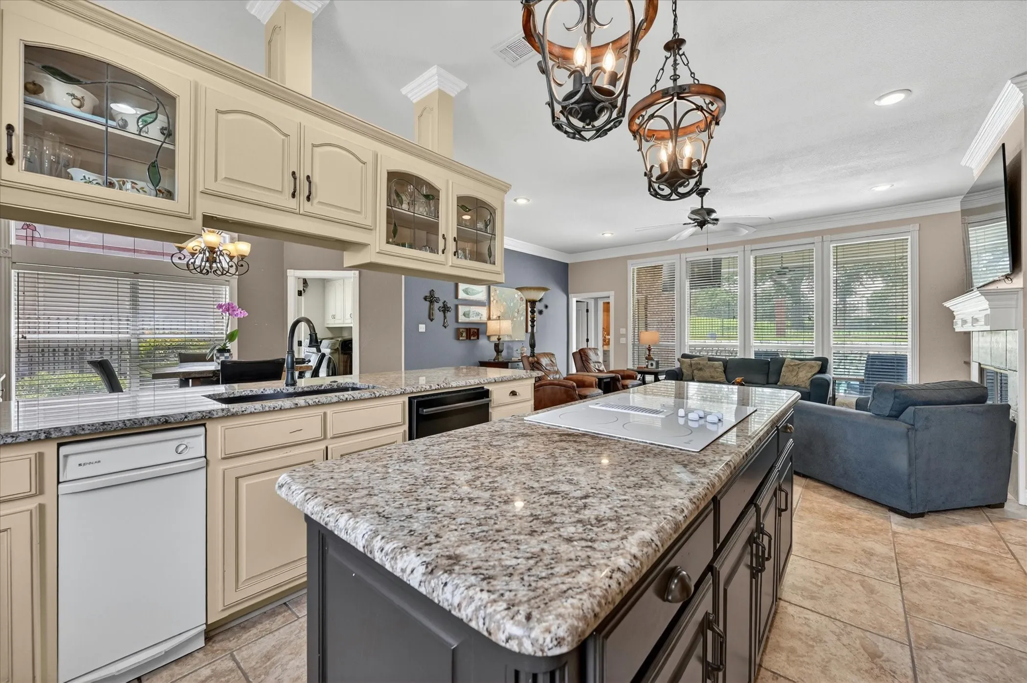 Gourmet kitchen featuring a large island with an integrated cooktop, granite countertops, tile flooring, custom cabinetry, and an open concept layout to the living area