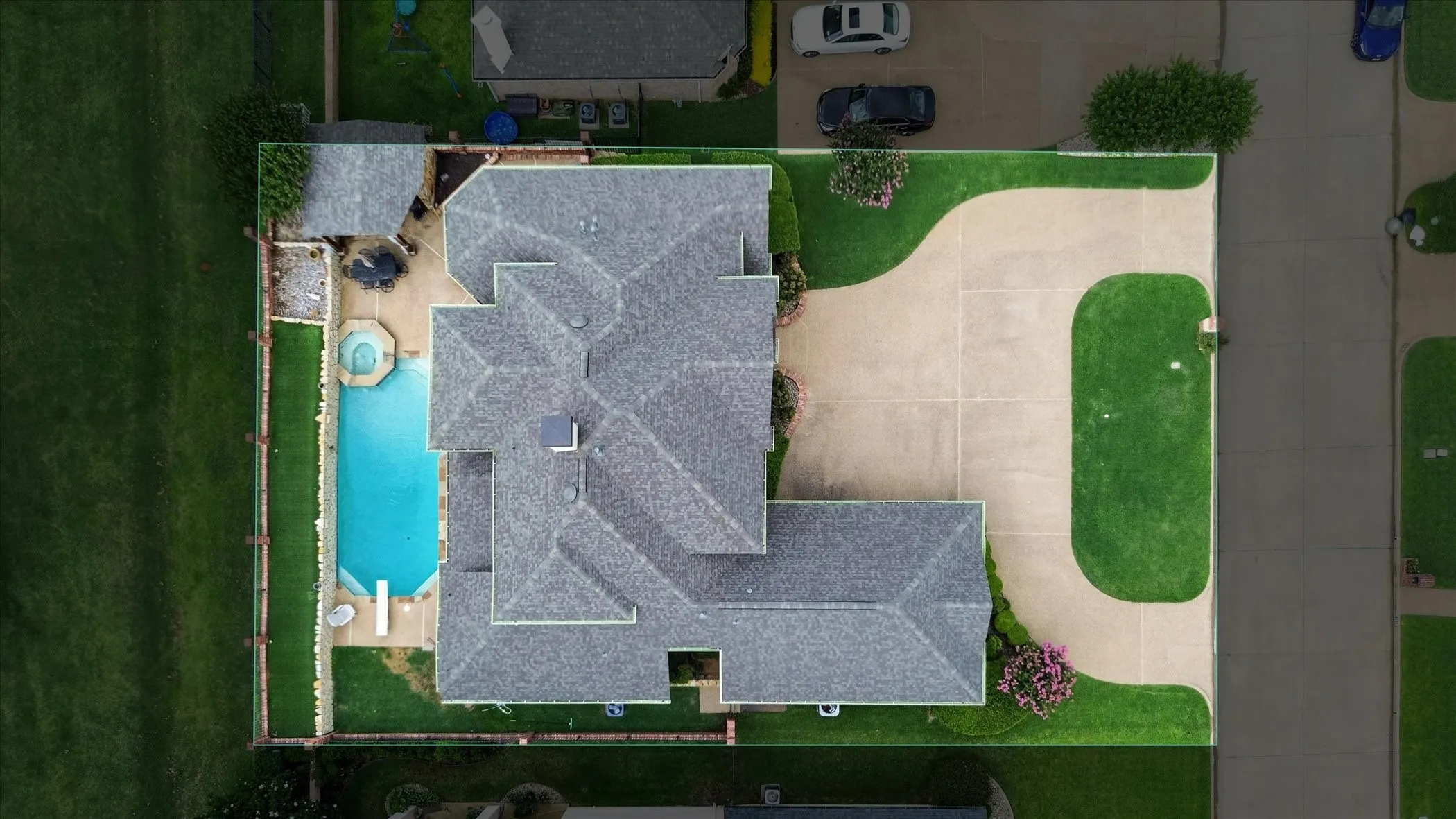 Asymmetrical roofline with gray shingles, large concrete driveway, expansive lawn, inground swimming pool, and an adjacent spa