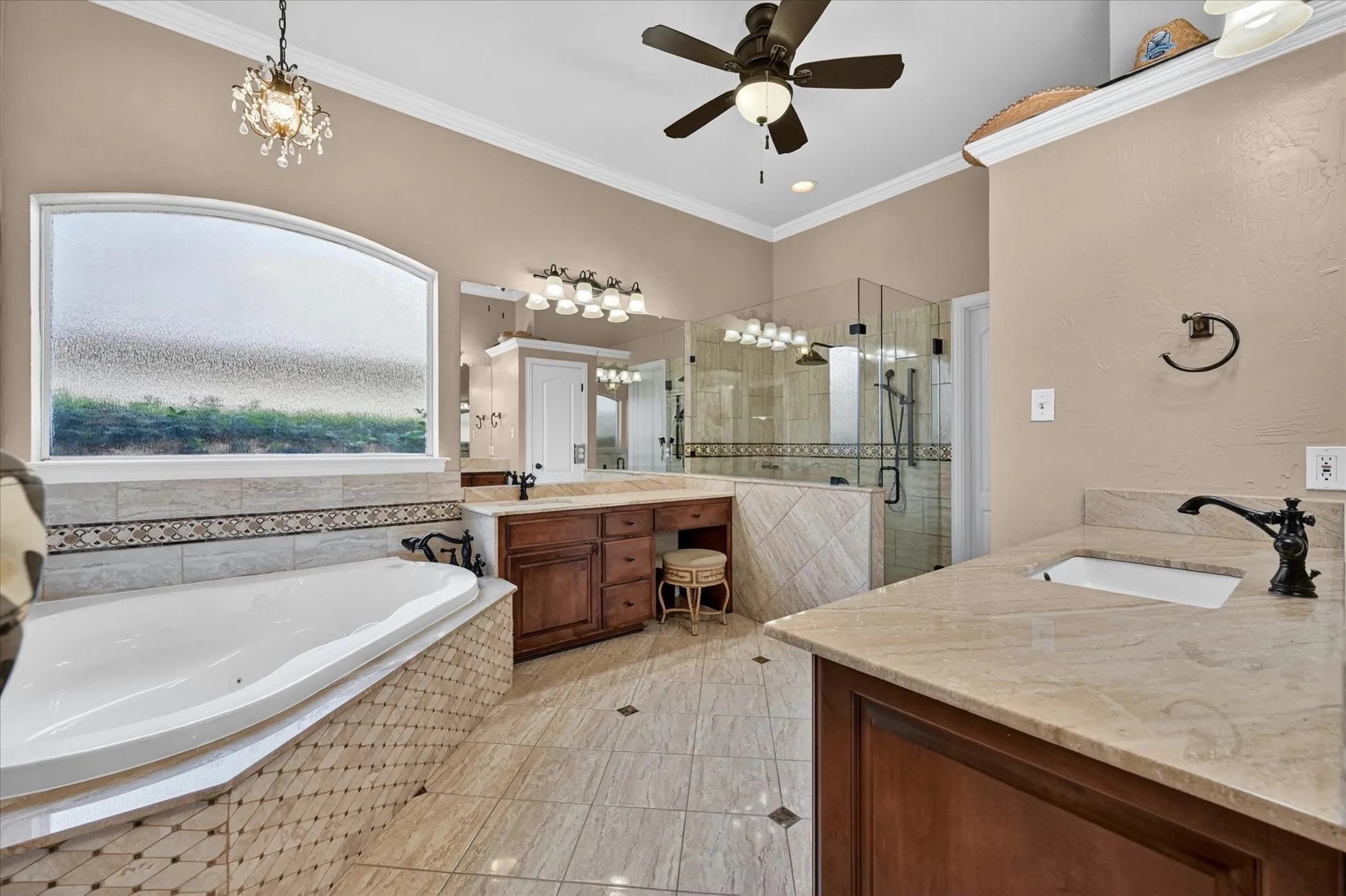 Spacious bathroom featuring a built-in jetted tub with tile surround, a glass-enclosed shower, dual vanity with undermount sinks and extensive countertop space, and tiled flooring with dark inlay accents