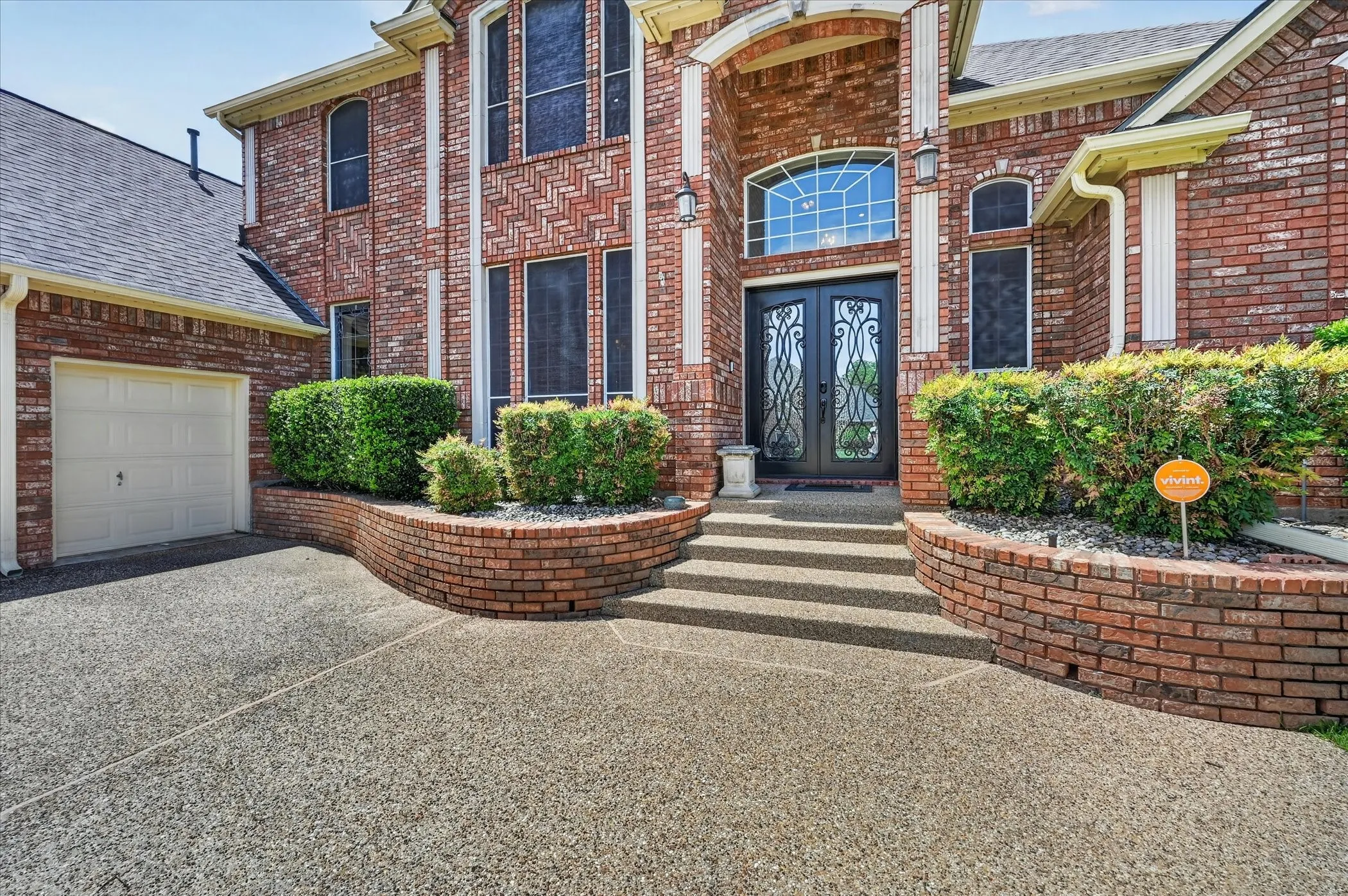Brick exterior facade with a two-story entryway featuring an arched window above double entry doors with decorative ironwork