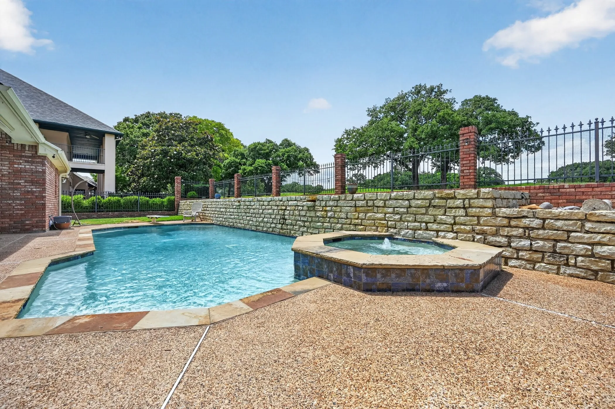 Outdoor oasis featuring a sparkling swimming pool with stone coping, an integrated spa with a fountain, and an exposed aggregate patio