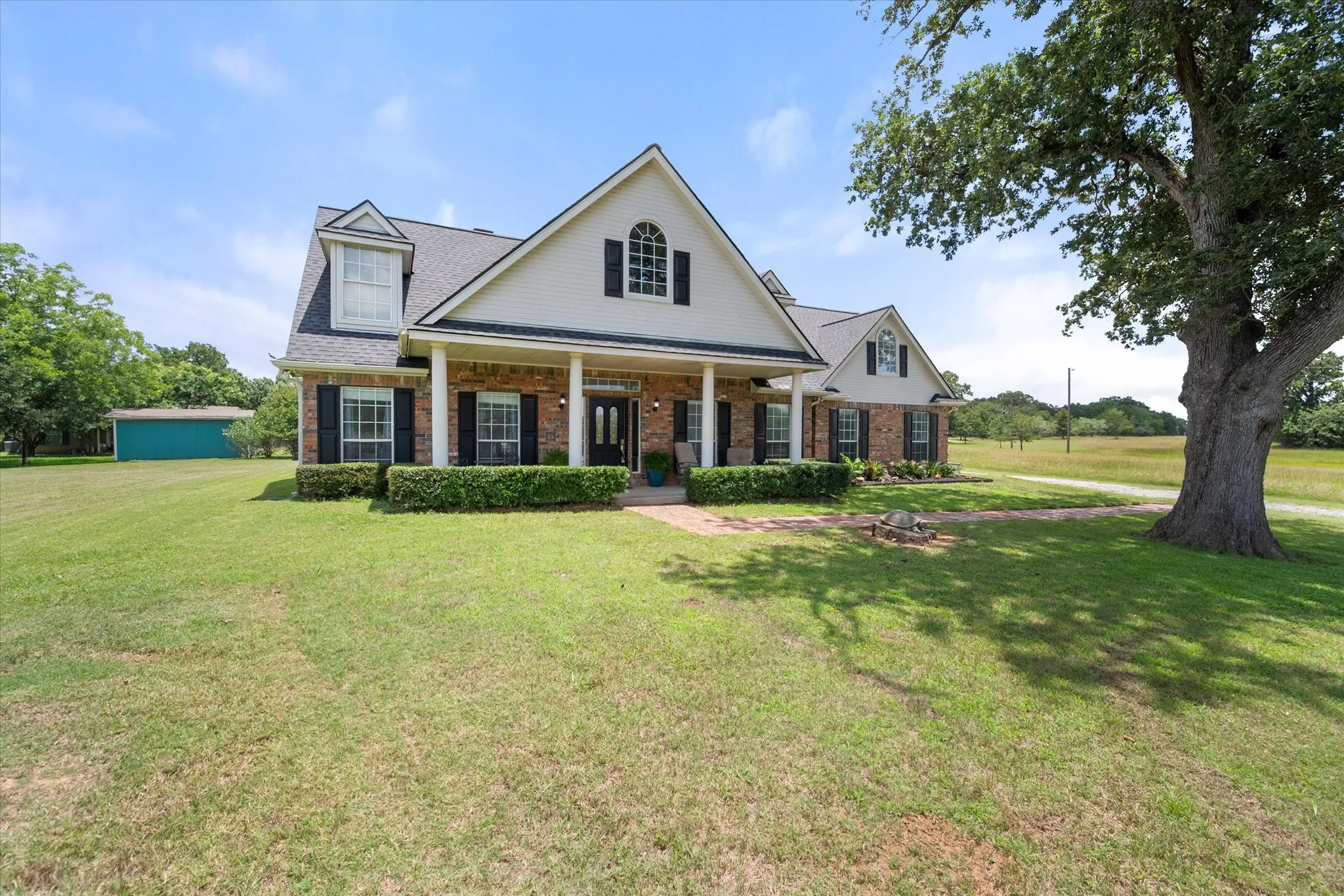 Front exterior near Dallas with brick curb appeal, covered porch, mature shade tree, and welcoming walkway.
