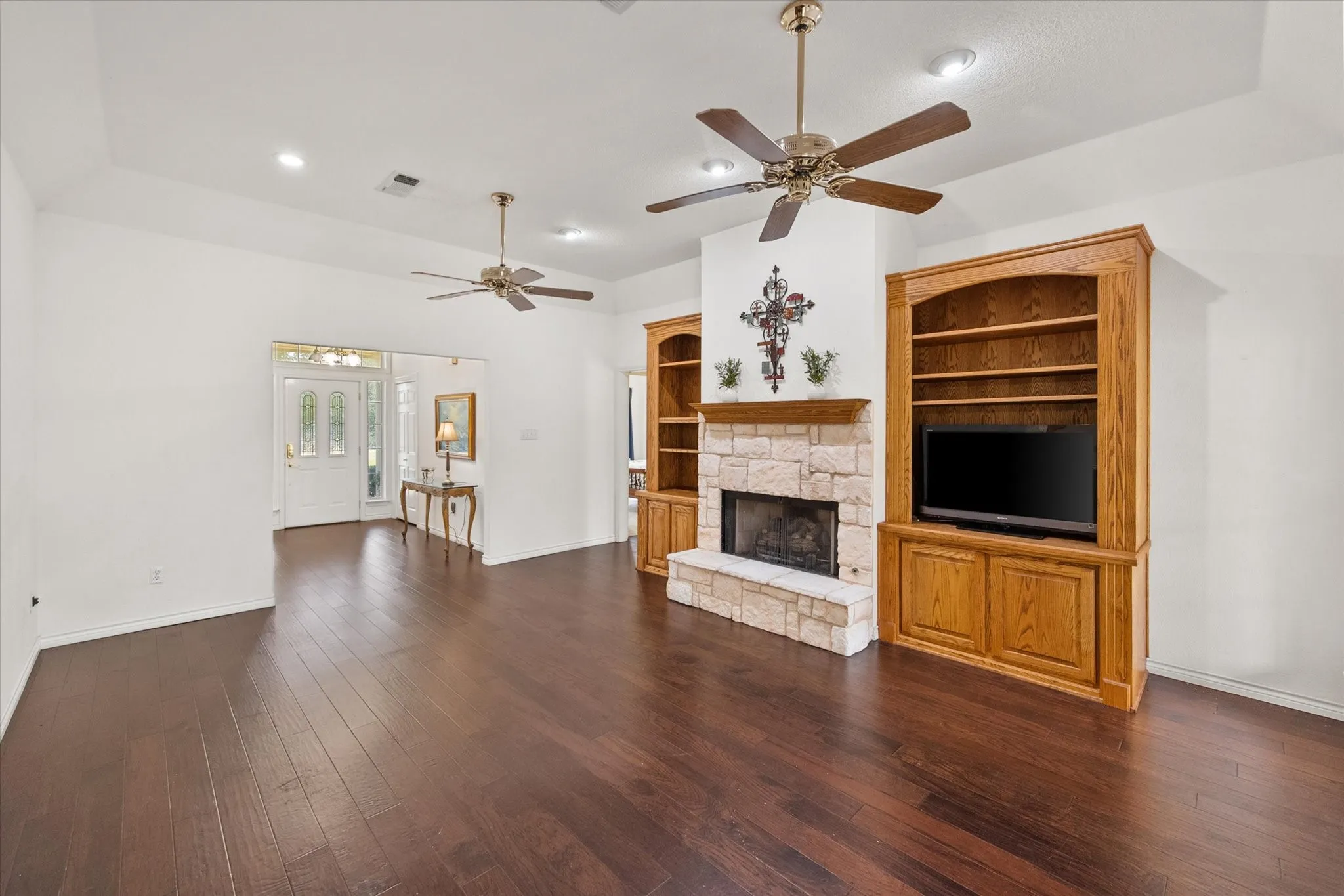 Spacious living room in Streetman, TX featuring a wood-burning fireplace, built-ins, ceiling fans, and access to the sunroom.