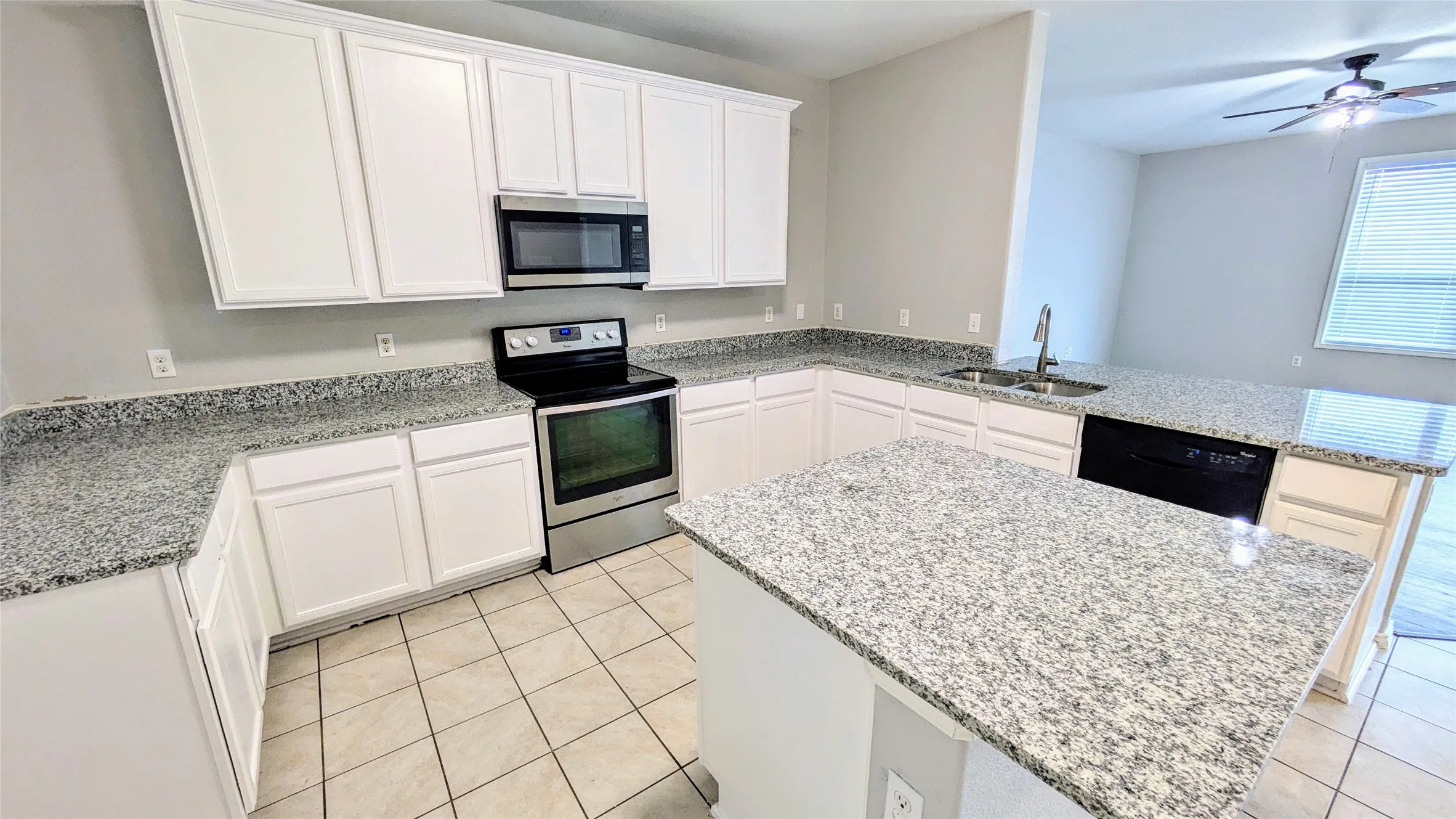 Bright kitchen featuring white cabinetry, granite countertops, stainless steel appliances, a center island, and tile flooring