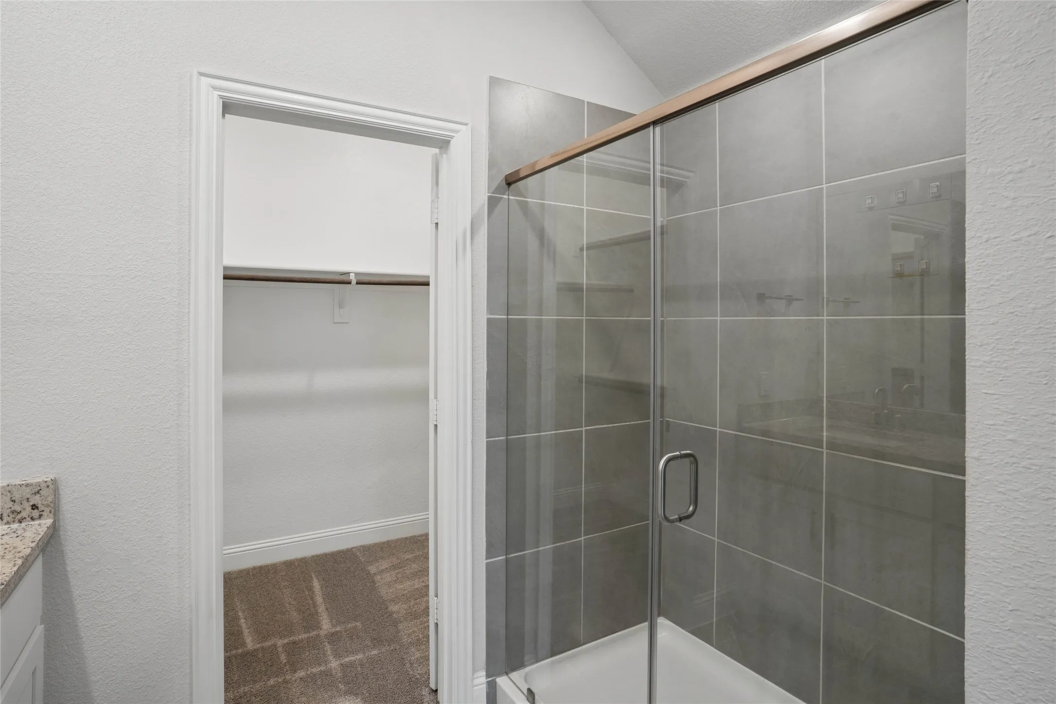 Glass-enclosed shower with gray square tile surround and bronze-finish framing