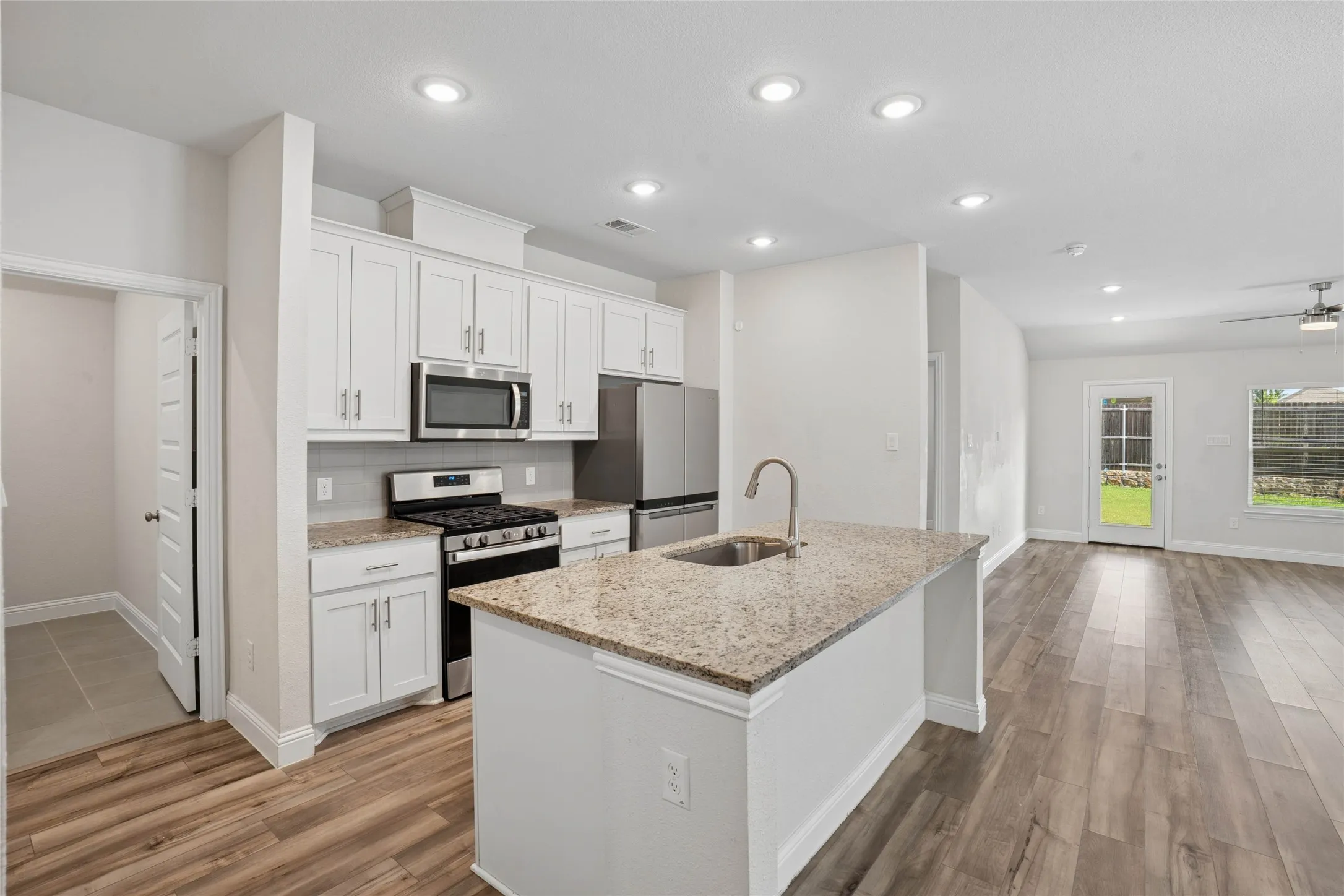 Modern kitchen featuring an island with an undermount sink, granite countertops, white cabinetry, stainless steel appliances, and wood-finish flooring