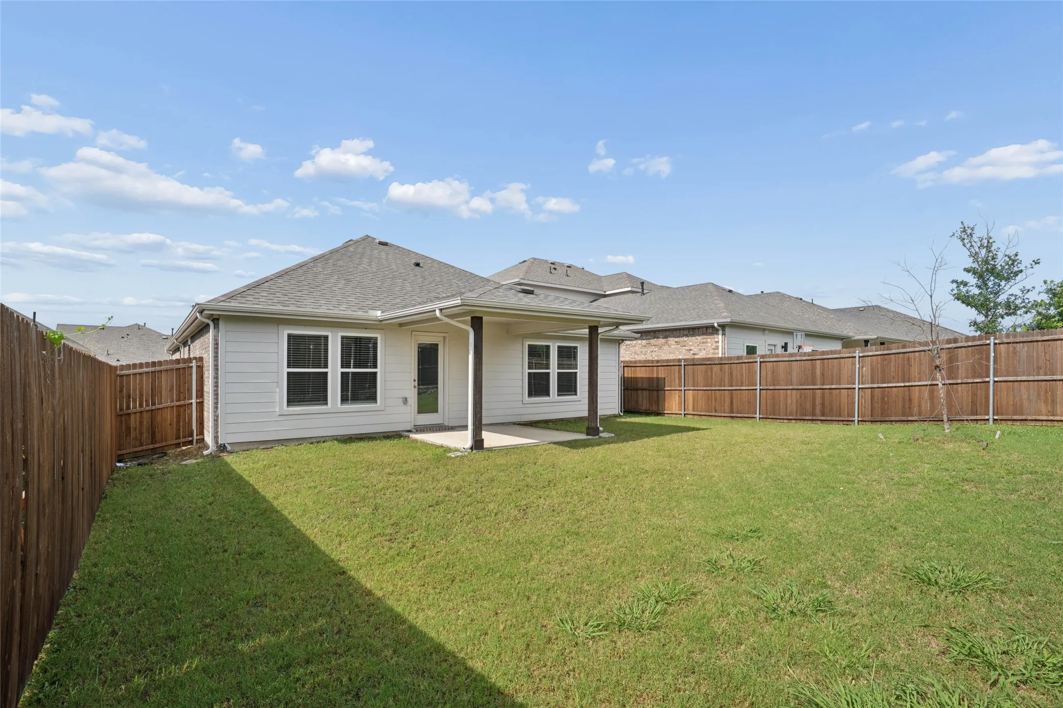 Spacious backyard featuring a covered patio, privacy fencing, a manicured lawn, and exterior siding with multiple windows