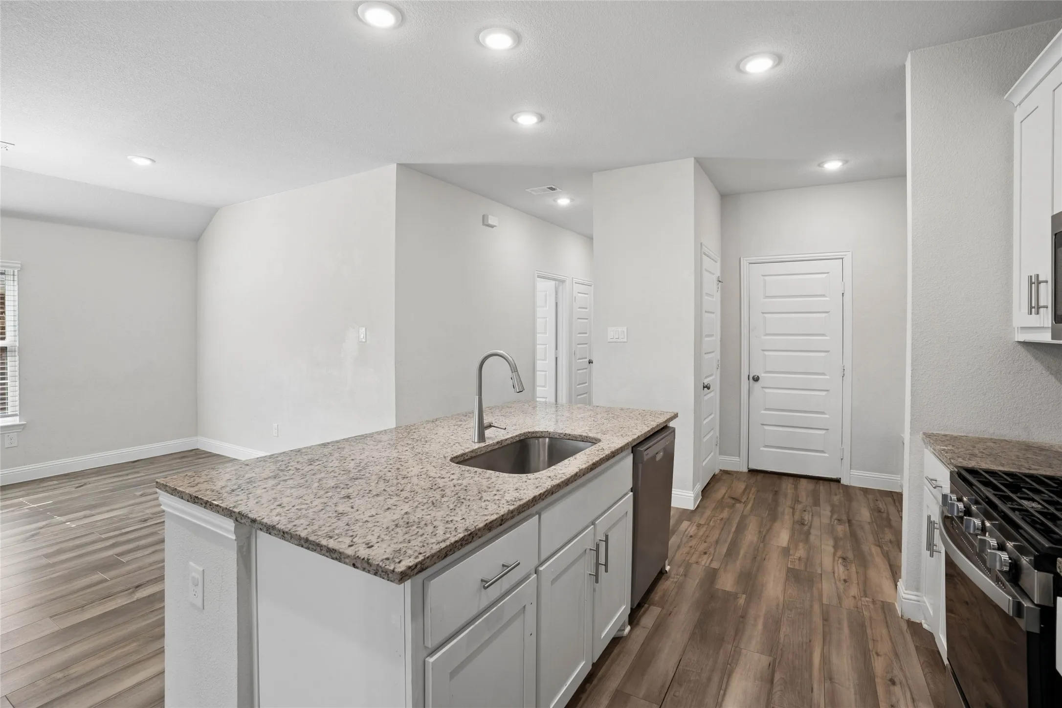 Kitchen island featuring a stainless steel sink with a gooseneck faucet, light granite countertop, and white cabinetry