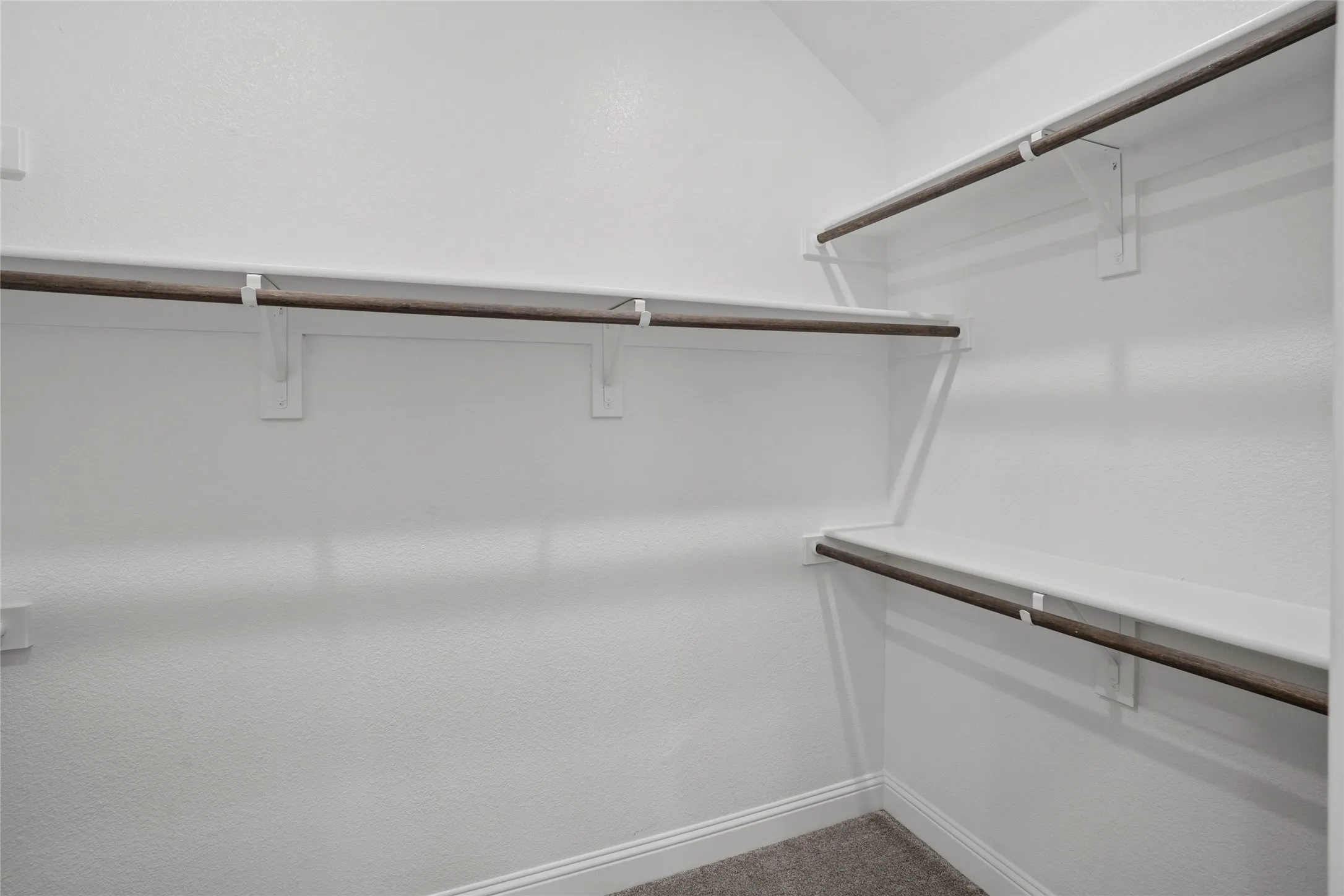 White-painted closet interior featuring multiple wooden hanging rods, white shelving, and white baseboards