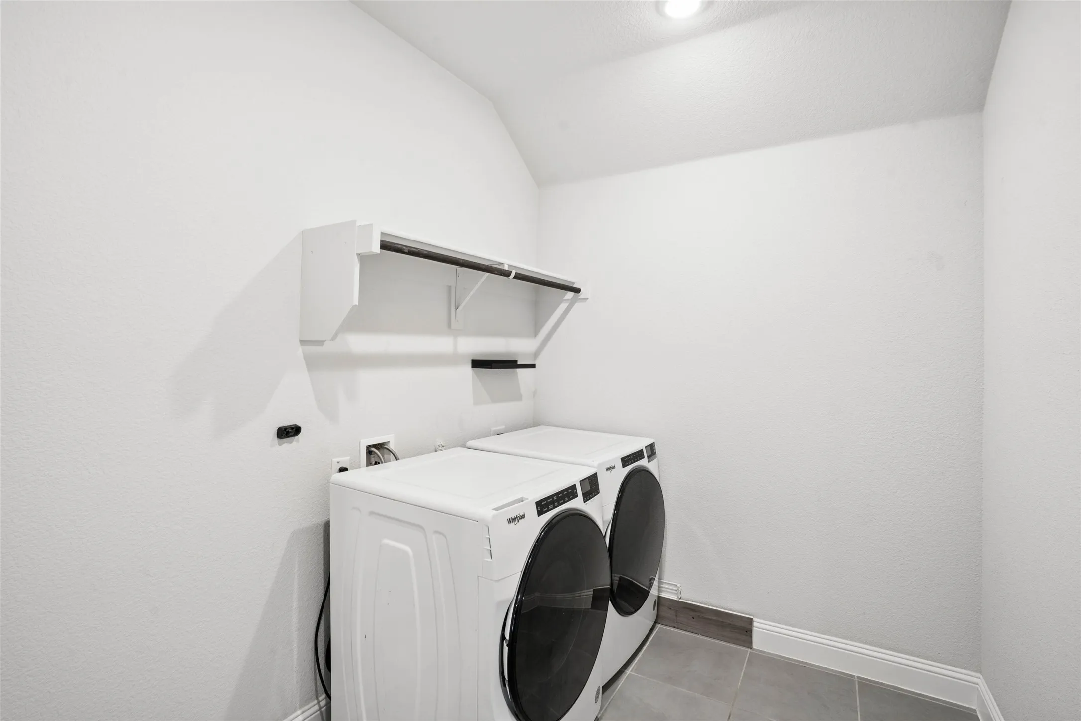 Dedicated laundry space featuring white textured walls, recessed ceiling lighting, a built-in shelf with a hanging rod, and grey tile flooring