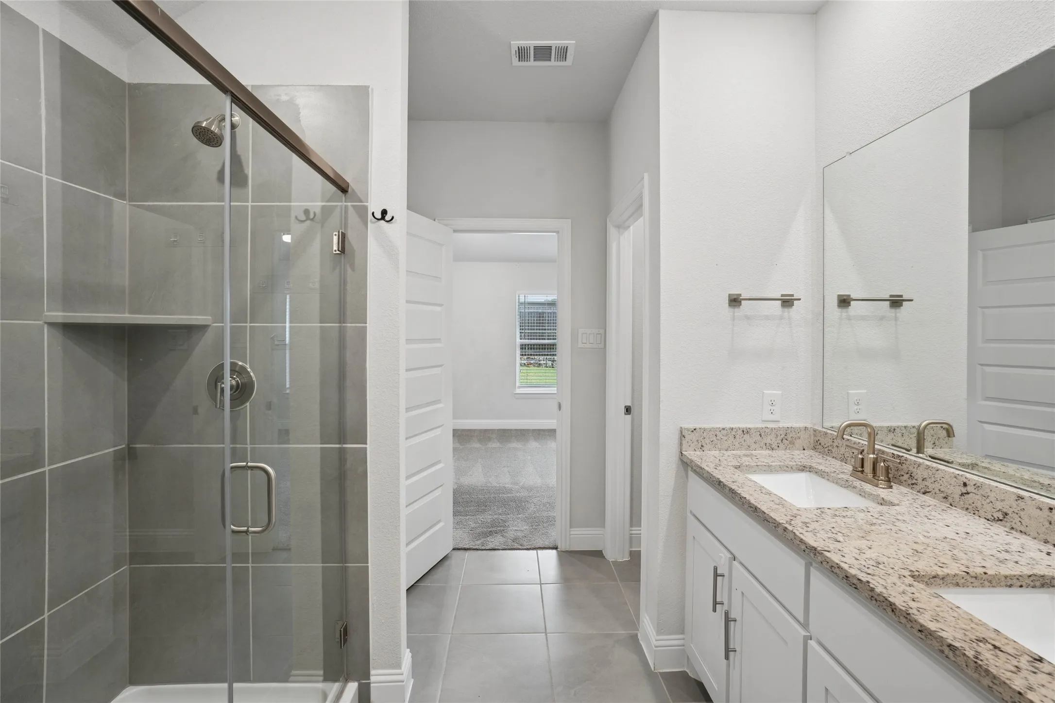 Bathroom featuring a glass-enclosed shower with tile surround, a dual vanity with light-toned countertops, and light-colored flooring
