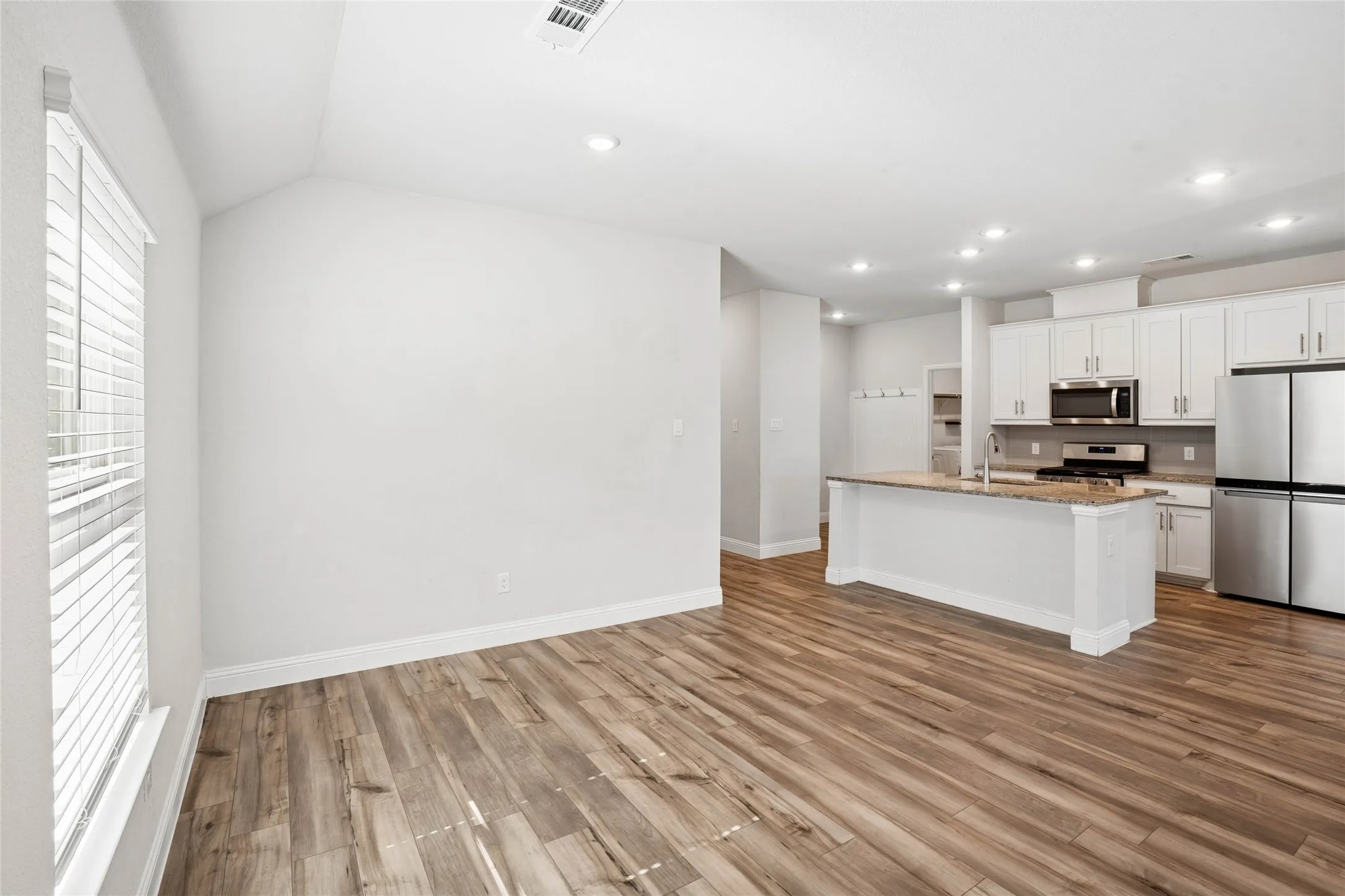 Open-concept living space featuring wood-finish flooring, recessed lighting, and a vaulted ceiling