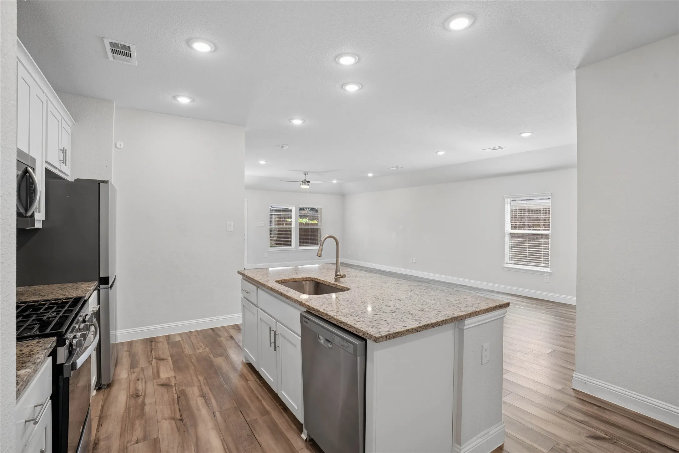 Open-concept kitchen featuring an expansive center island with an undermount sink, granite-style countertops, white cabinetry, and wood-finish flooring