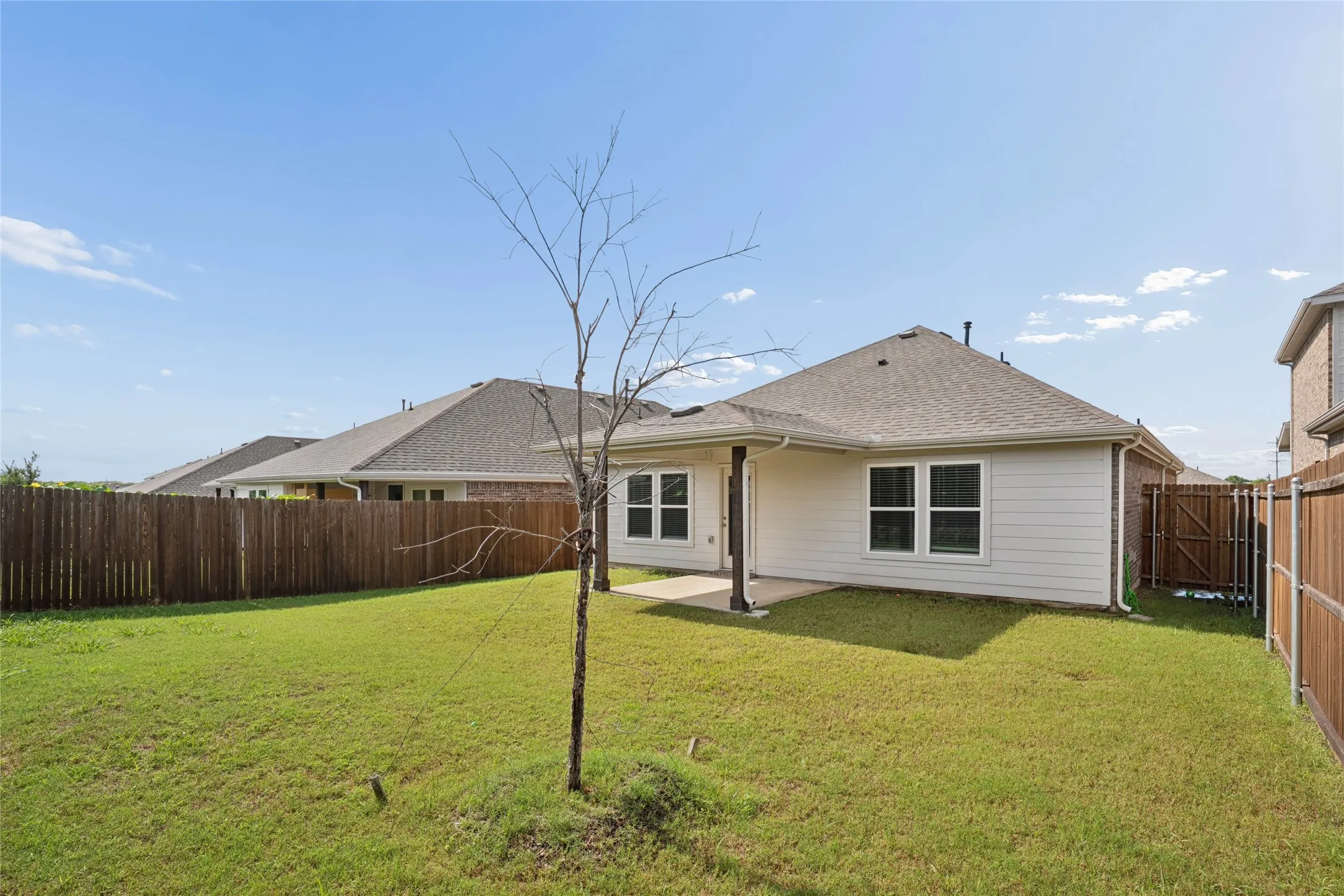 Expansive backyard featuring a green lawn, wood privacy fencing, and a covered patio with a concrete slab
