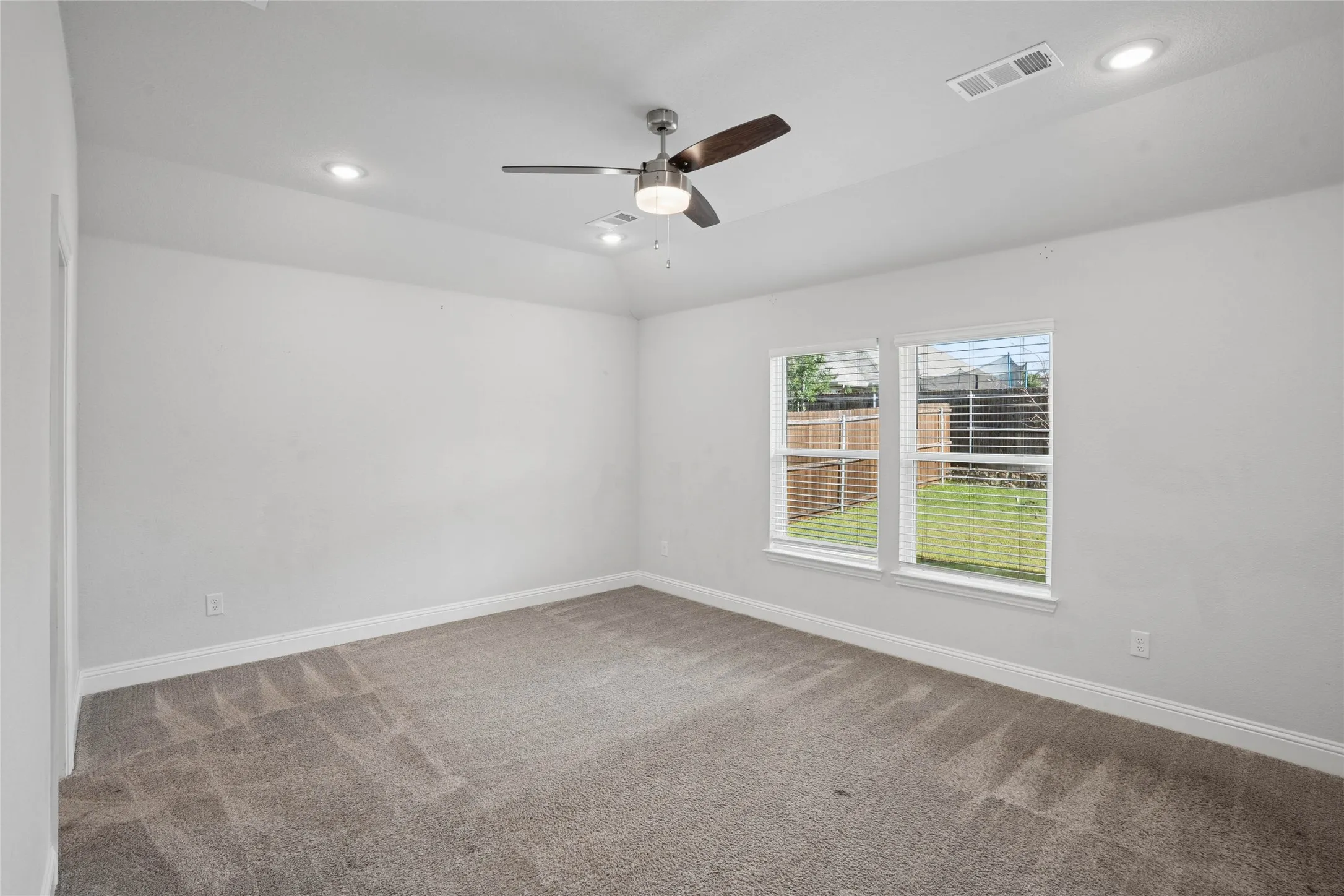 Spacious room featuring neutral carpeting, a ceiling fan with integrated lighting, recessed lighting, and a dual-pane window overlooking a fenced yard