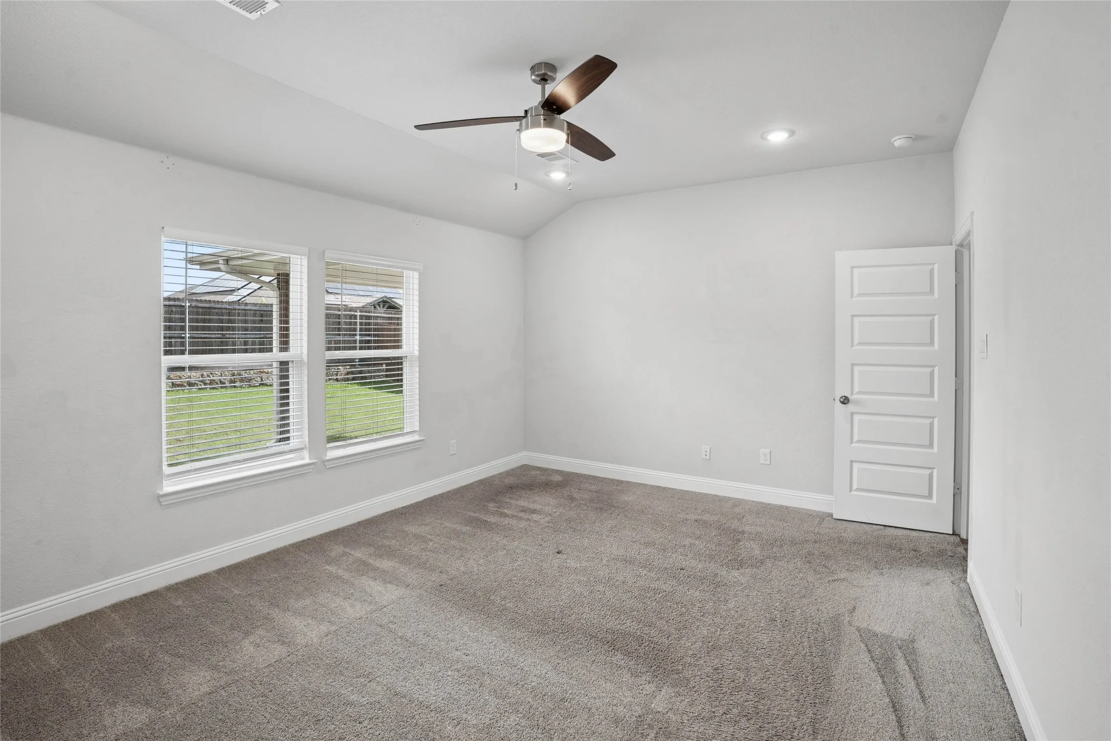 Carpeted room featuring dual windows with blinds, a five-panel interior door, a ceiling fan with integrated lighting, and recessed ceiling lights