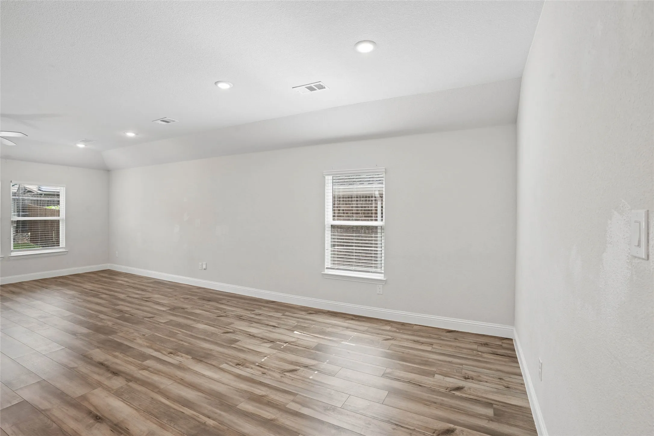 Spacious room featuring wood-finish flooring, white baseboards, and neutral wall paint