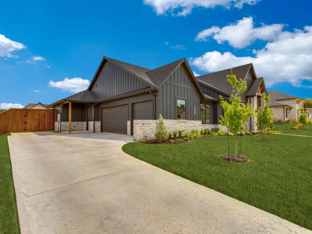 Contemporary exterior featuring dark vertical siding, stone accents, a two-car garage, and an extended driveway