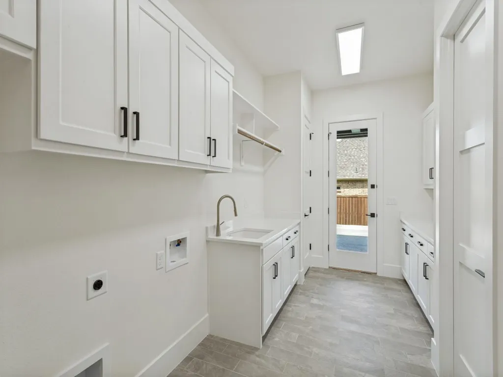 Dedicated utility room featuring white cabinetry with matte black hardware, a built-in sink, and tile flooring