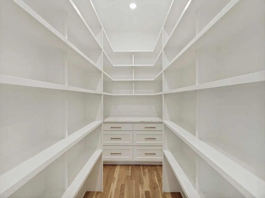 Walk-in pantry featuring extensive white shelving, a built-in cabinet with drawers, a light-toned countertop, and wood-finish flooring