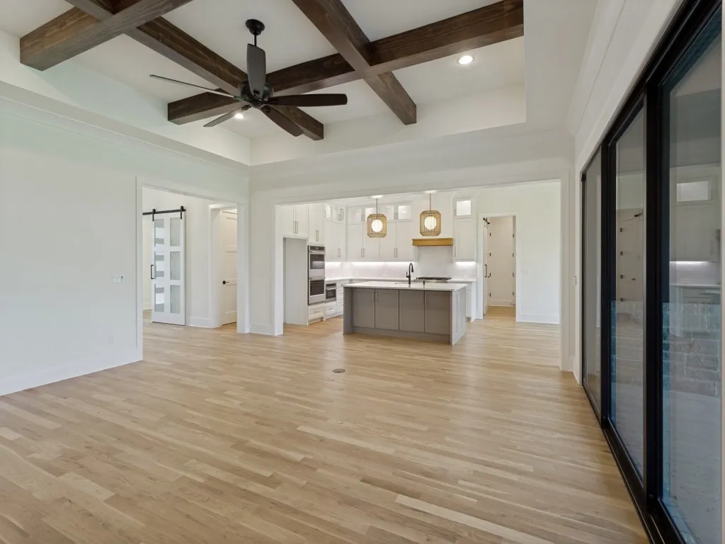 Open-concept living area featuring light wood-finish flooring, a coffered ceiling with dark wood beams, and a black ceiling fan