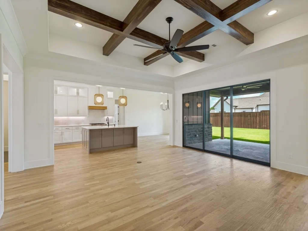 Spacious living area featuring light wood-finish flooring, a coffered ceiling with dark wood beams, and an integrated ceiling fan