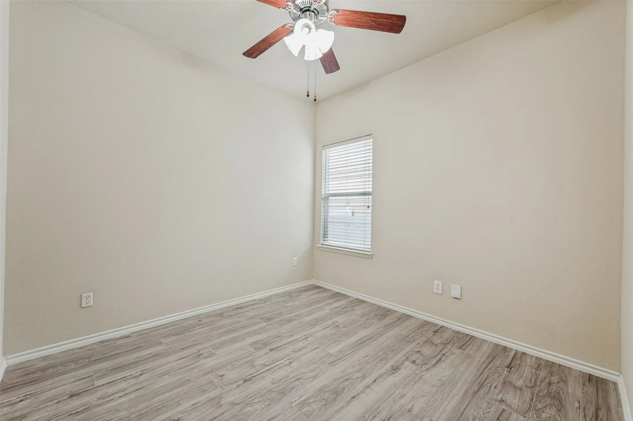 Neutral-toned room featuring wood-finish flooring and a ceiling fan with light fixture