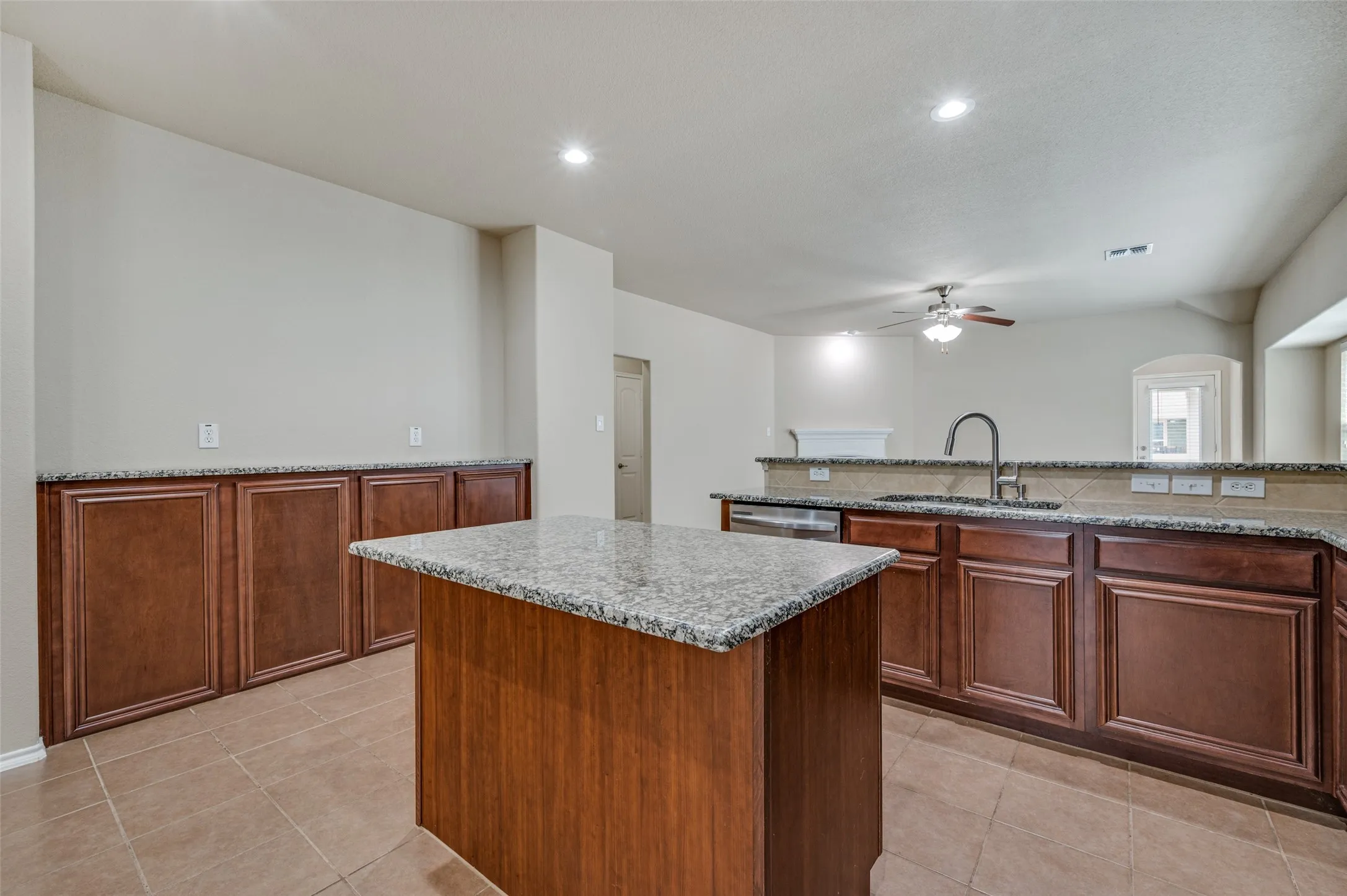 Kitchen featuring an island with granite countertop, rich wood-finish cabinetry, stainless steel dishwasher, and a gooseneck faucet