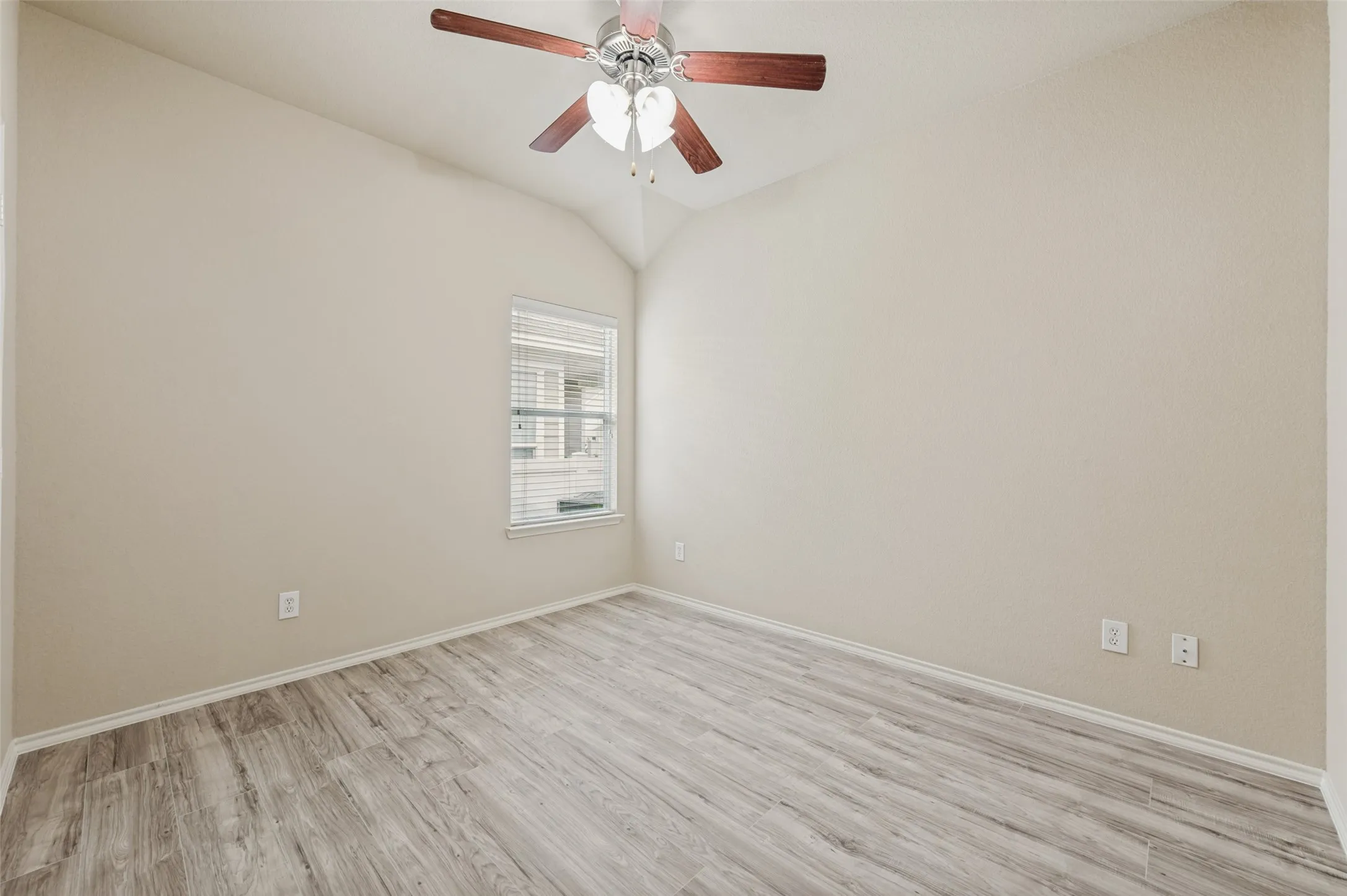 Spacious room featuring vaulted ceilings, wood-finish flooring, a window with blinds, and a ceiling fan