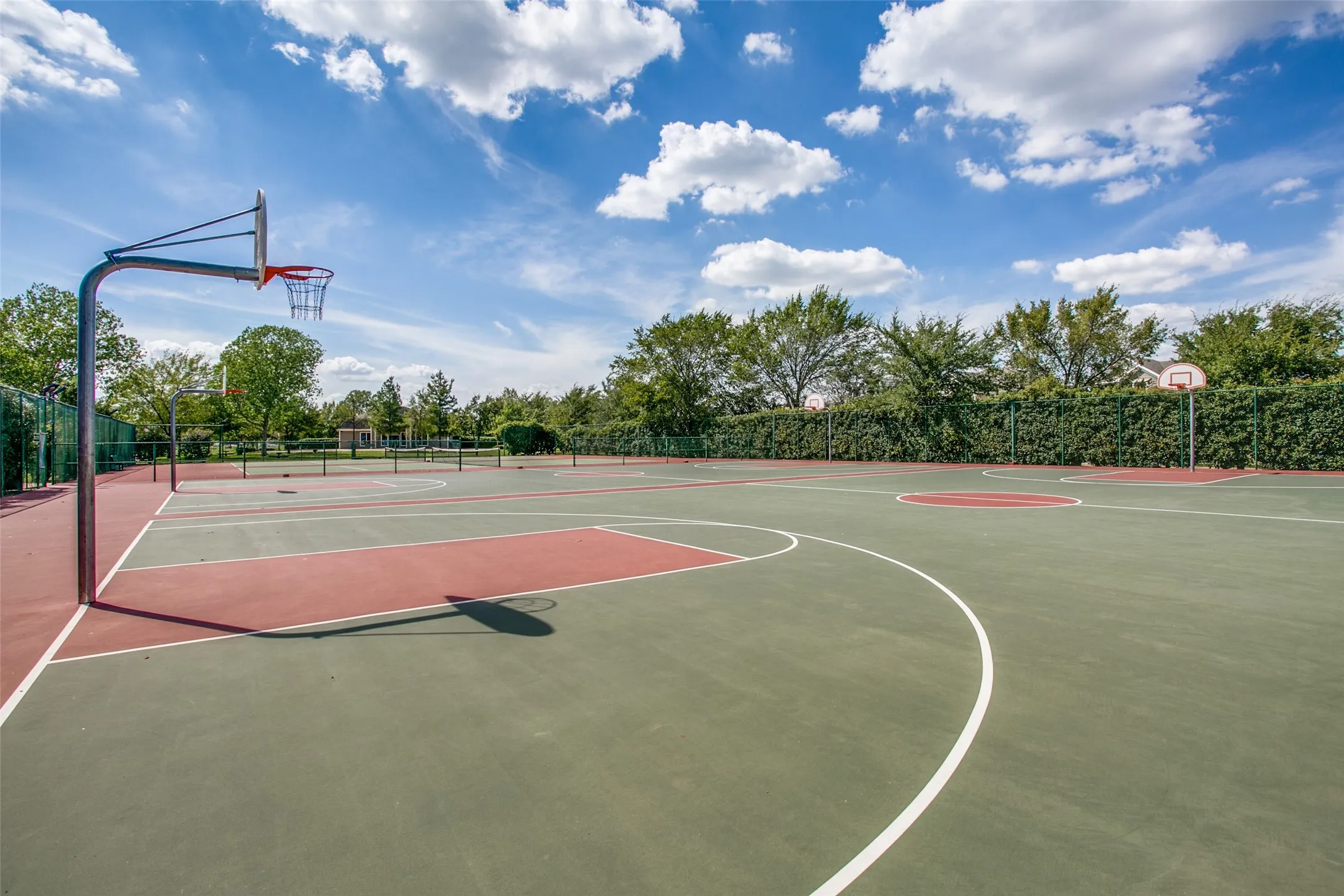 Multi-sport court featuring dedicated basketball hoops and clearly marked court lines, surrounded by lush green landscaping