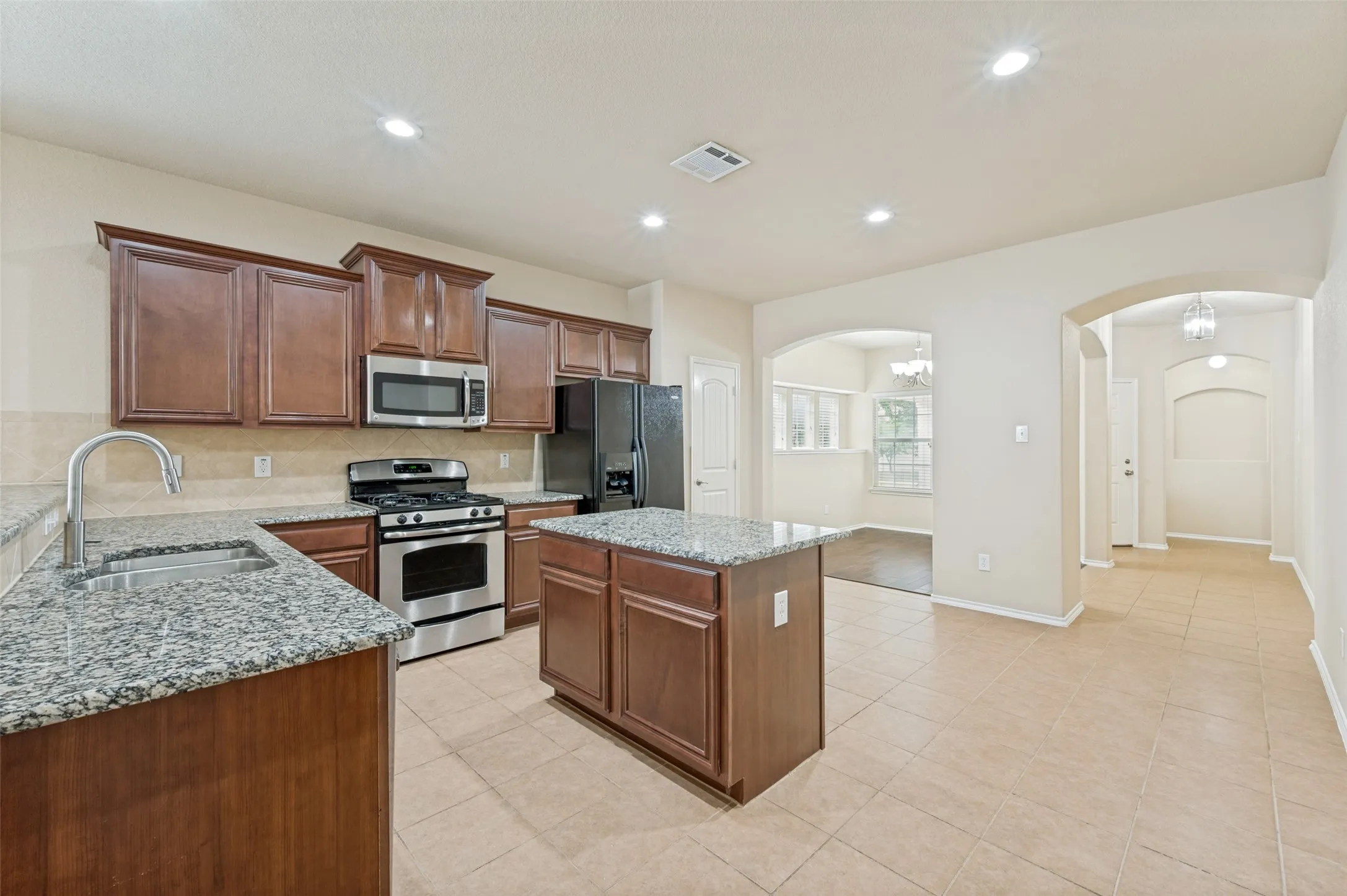 Kitchen featuring wood cabinetry, granite countertops, stainless steel appliances, a center island, and tile flooring