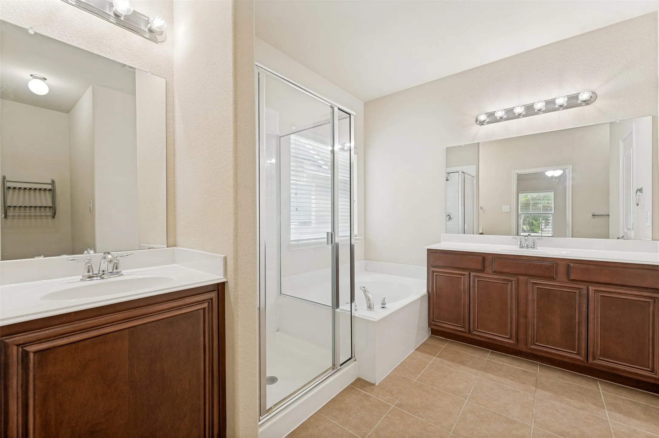 Bathroom featuring a glass-enclosed shower, a built-in tub, dual vanity with wood-finish cabinetry, and tiled flooring