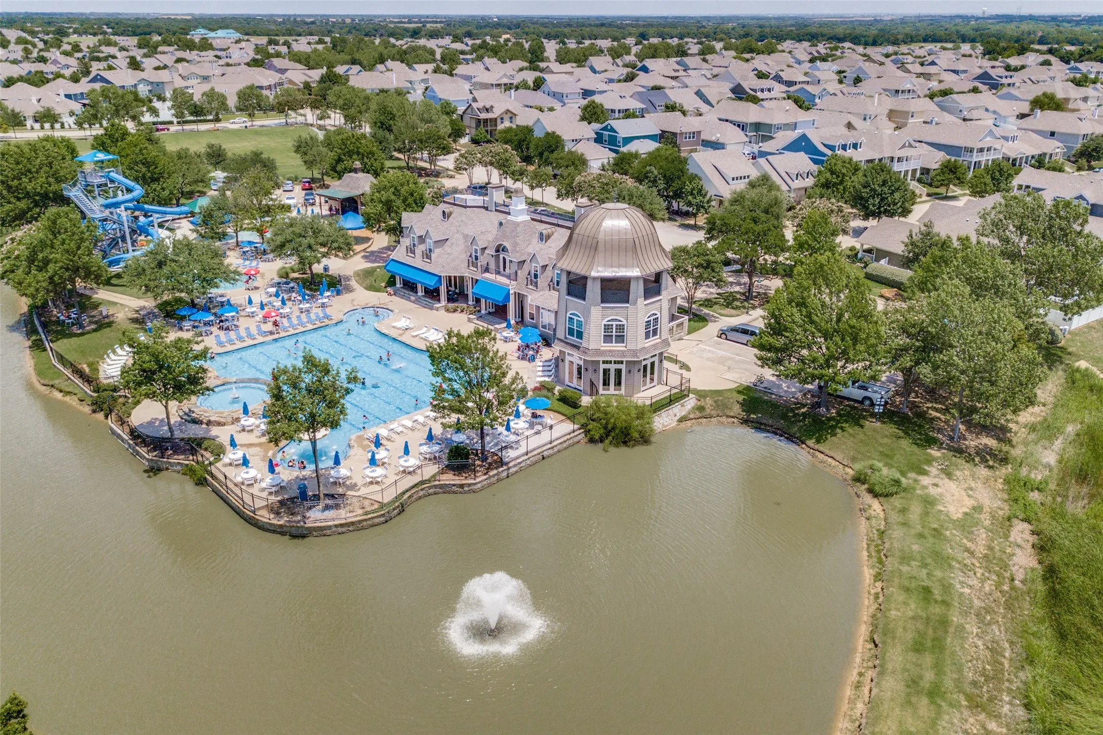 Lakeside community amenities featuring a multi-level swimming pool, water slides, a fountain, mature trees, and a grand, domed building