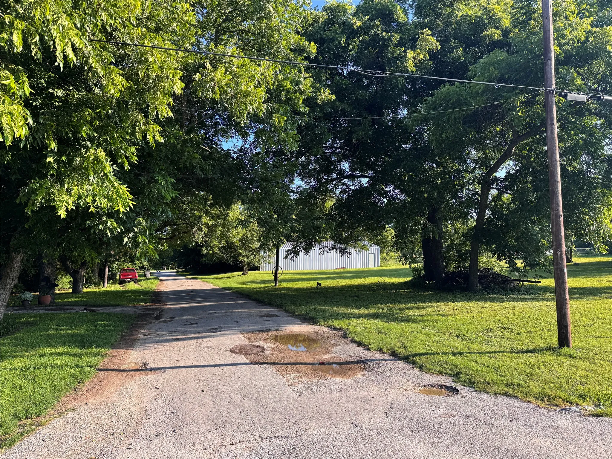 Paved driveway extending into the property, bordered by mature trees and verdant lawns