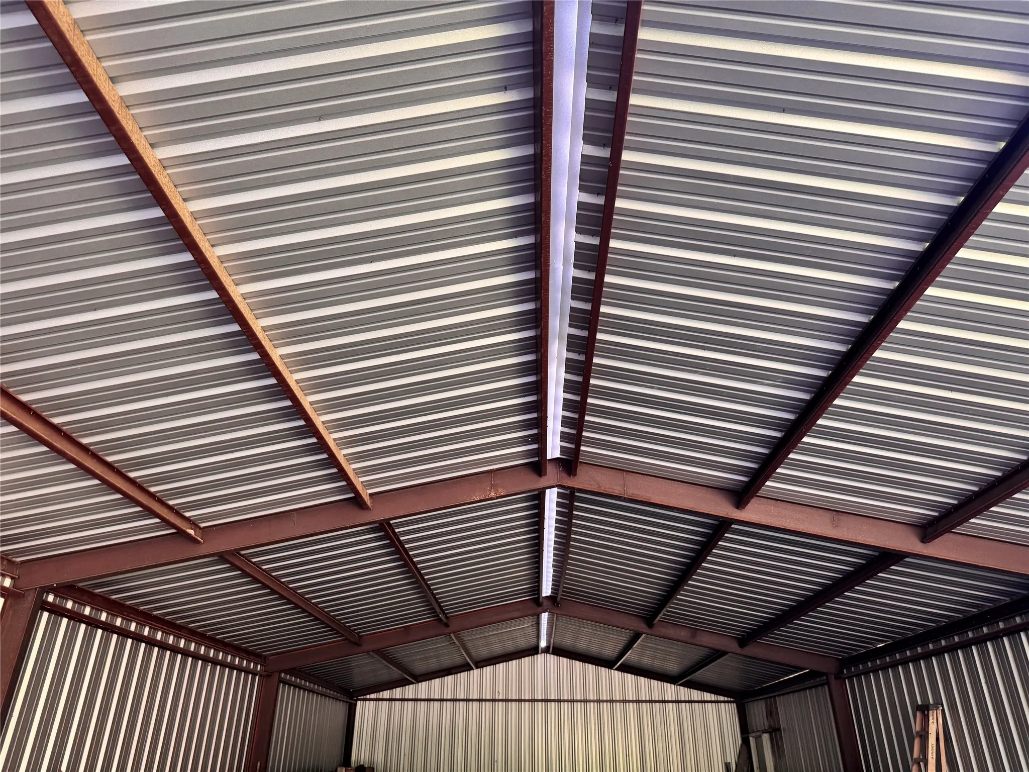 Corrugated metal roof with exposed structural beams and integrated fluorescent lighting