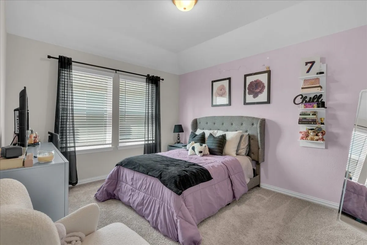 Carpeted bedroom featuring a gray upholstered headboard, multiple windows with blinds and sheer drapes, a built-in ceiling light, and wall-mounted shelving