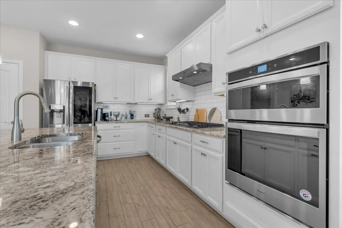 Kitchen featuring white cabinetry, stone-finish countertops, subway tile backsplash, stainless steel appliances, and wood-finish flooring