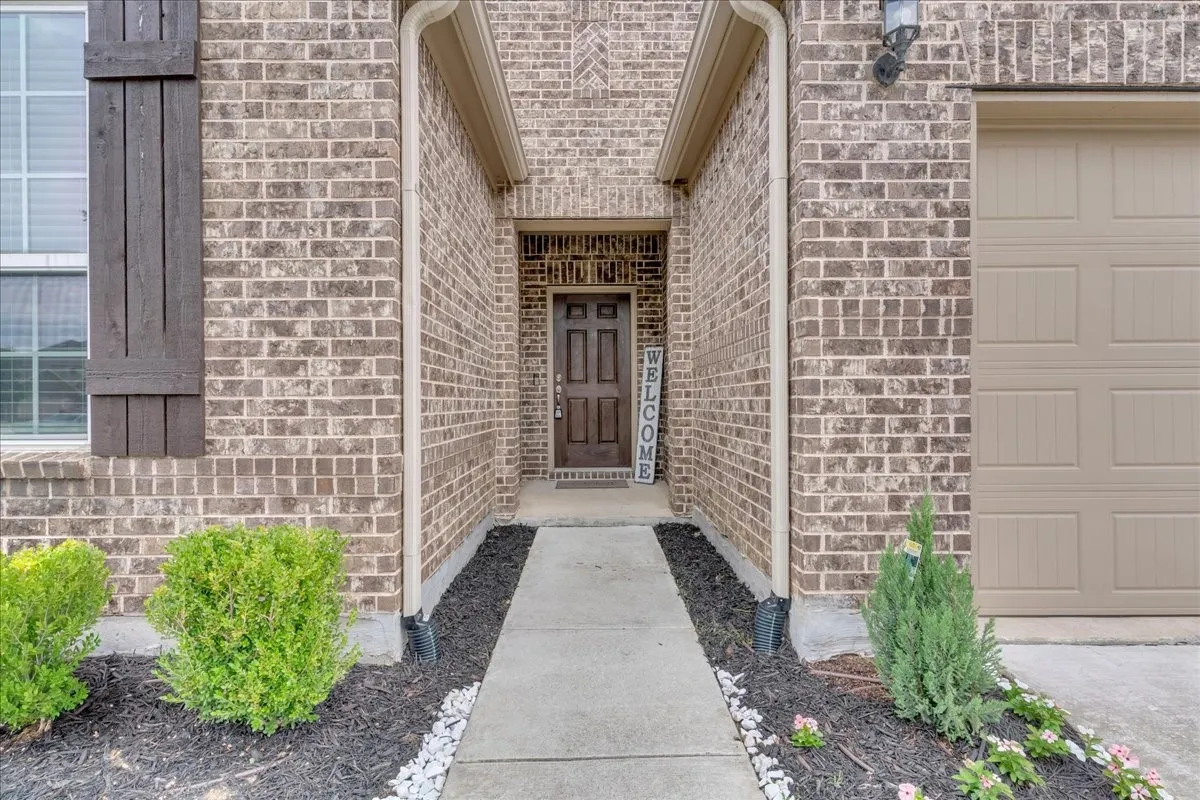 Brick facade with dark wood shutters, featuring a covered entry and a concrete walkway