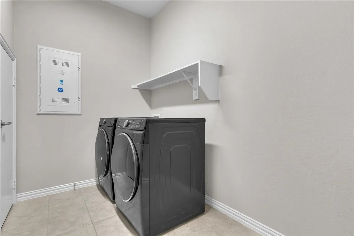 Dedicated utility space featuring tile flooring, neutral wall tones, a white wall-mounted shelf, and baseboard trim